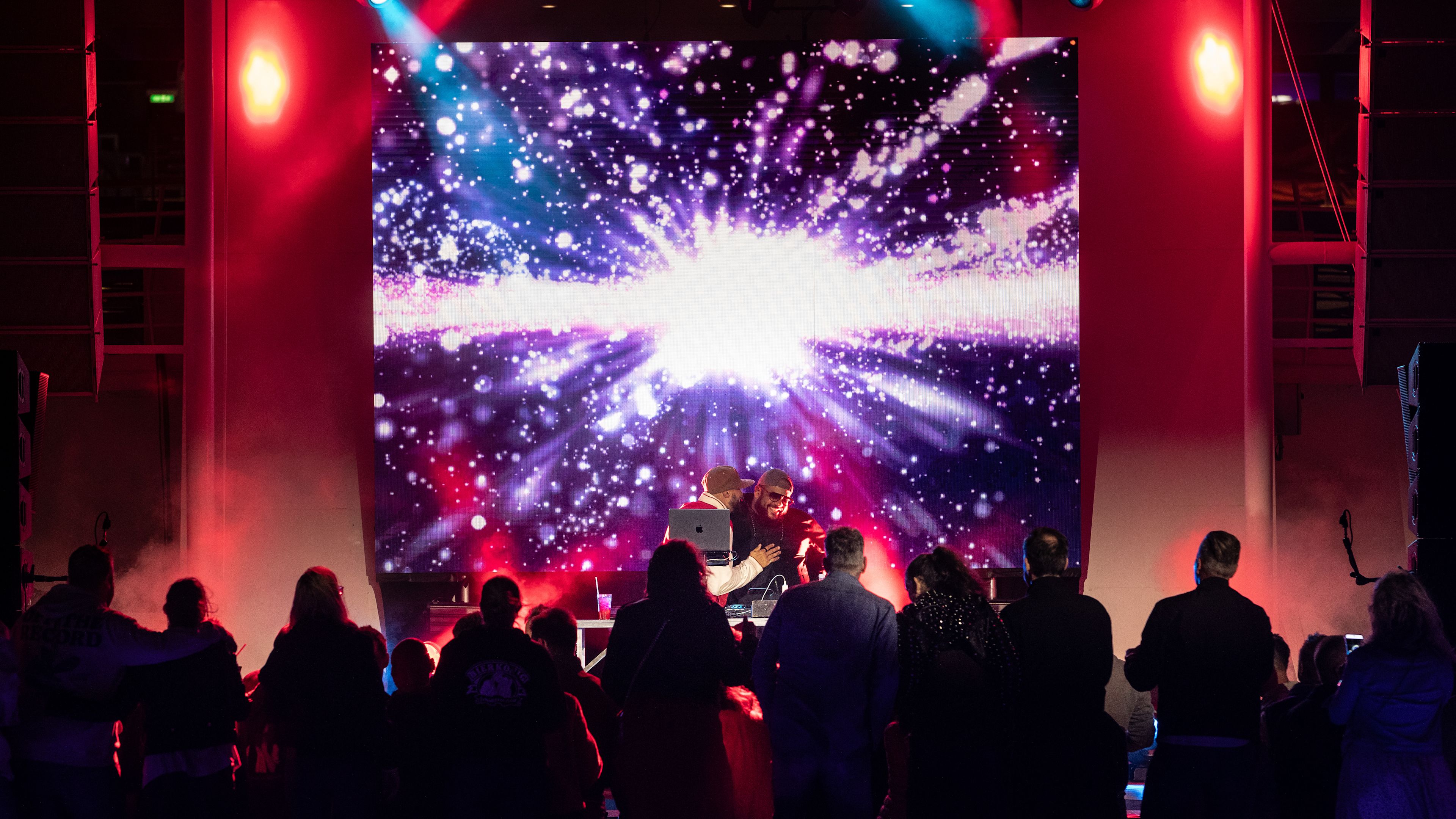 Millennium Faiz DJ Lionel Richard Menschenmenge vor bunter Bühne mit Lichteffekten und DJ.