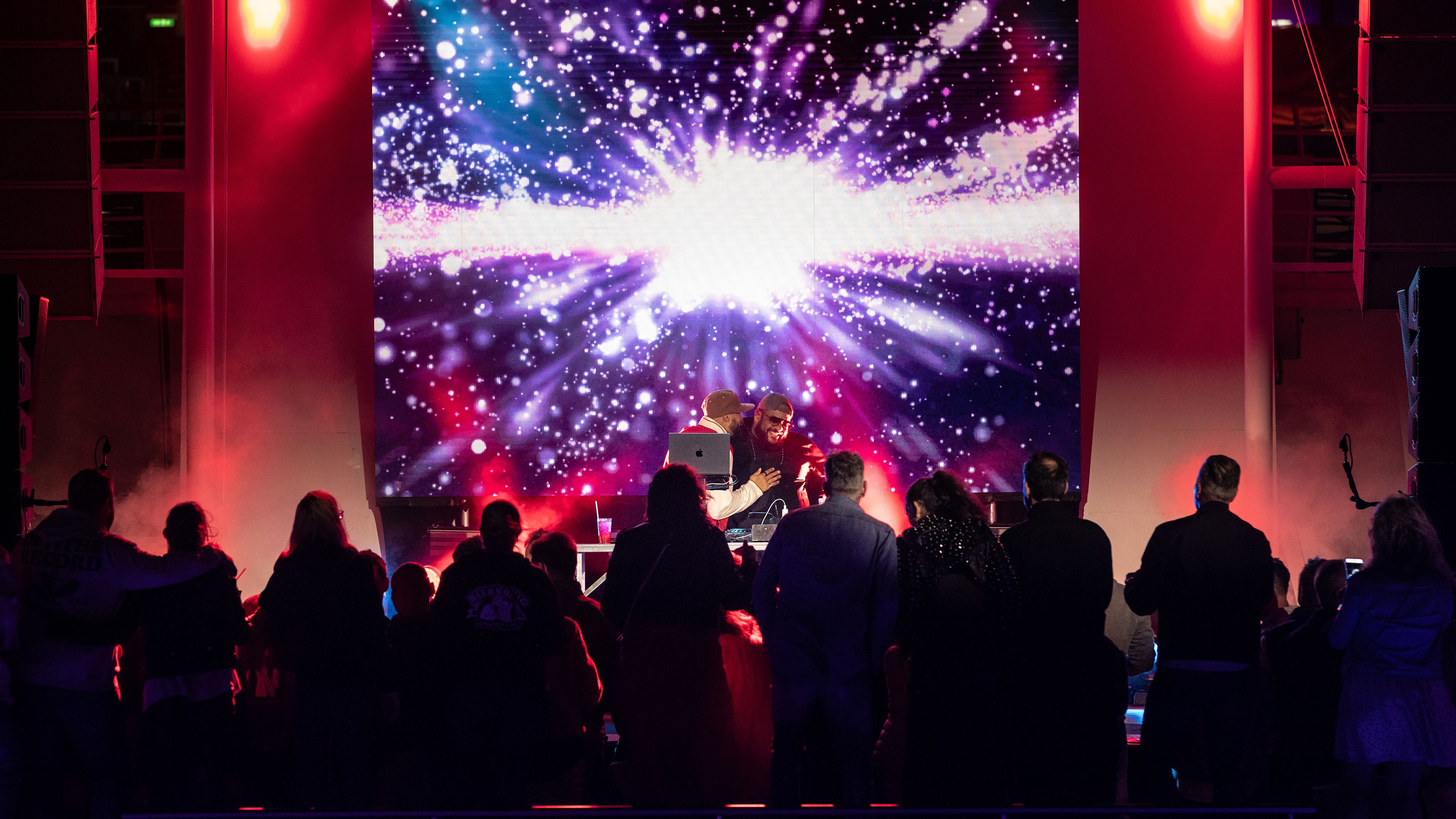 Menschenmenge vor bunter Bühne mit Lichteffekten und DJ. Menschenmenge vor bunter Bühne mit Lichteffekten und DJ.