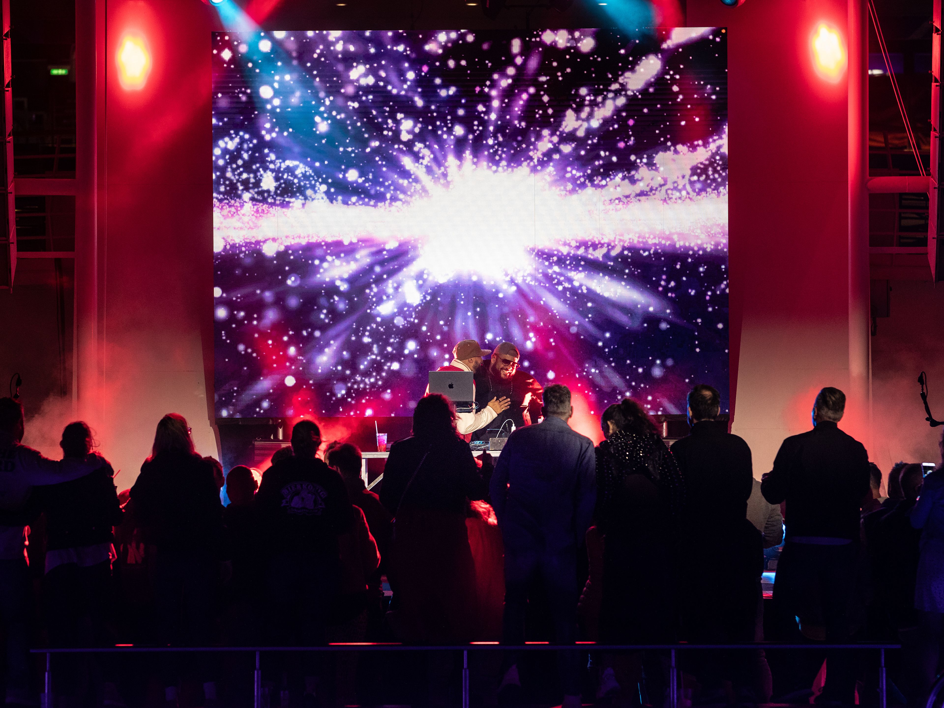 Menschenmenge vor bunter Bühne mit Lichteffekten und DJ. Menschenmenge vor bunter Bühne mit Lichteffekten und DJ.