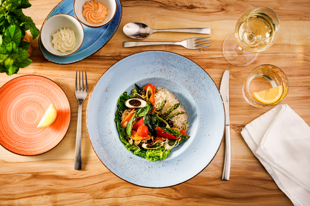 Bunter Salat mit Reis auf blauem Teller, Holztisch.