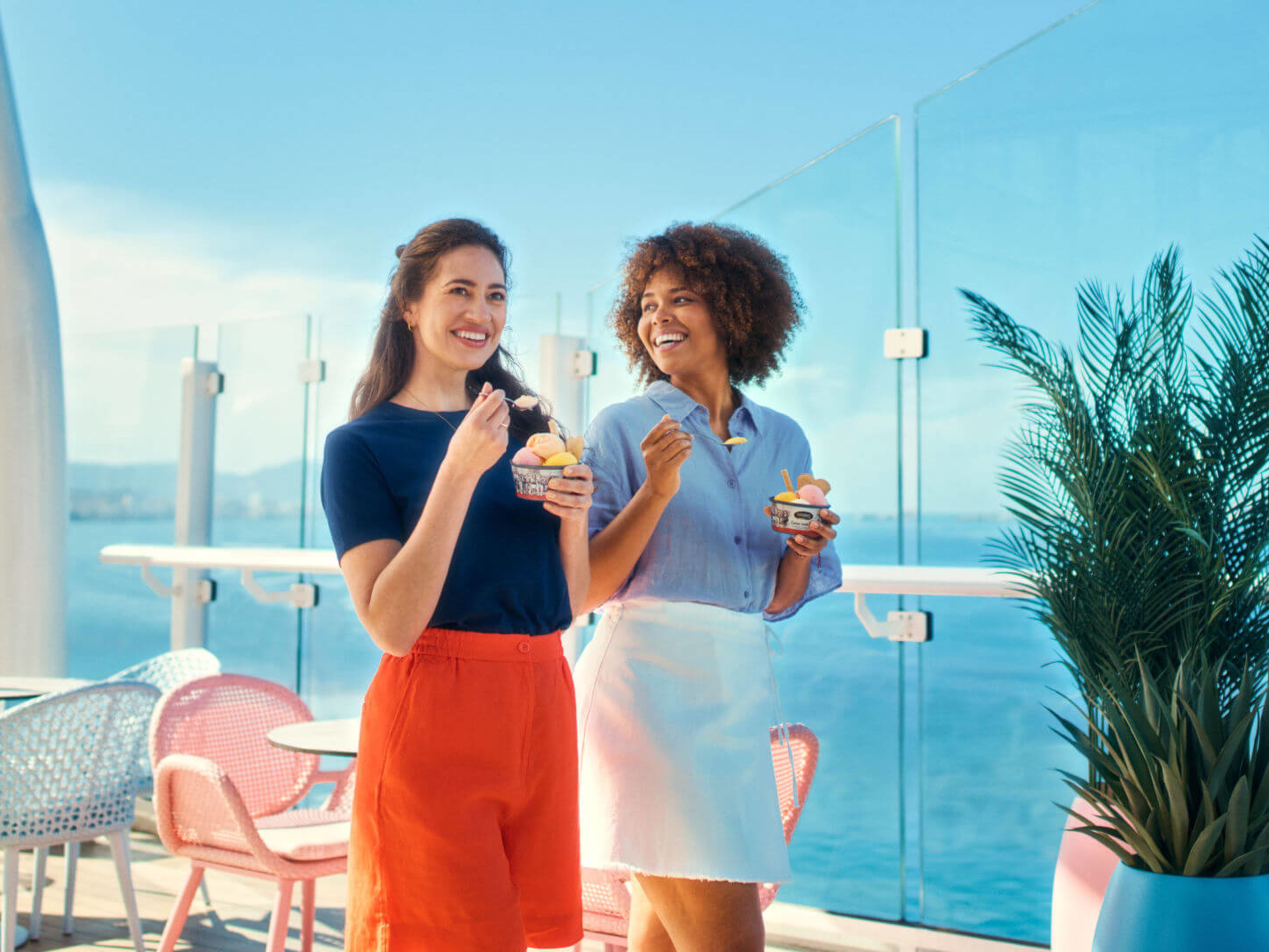 Spaziergang auf dem Außendeck mit Premium-Eis Bruno Gelato Zwei Frauen essen Eis auf Kreuzfahrtschiff der Mein Schiff® Flotte, sonniger Tag.