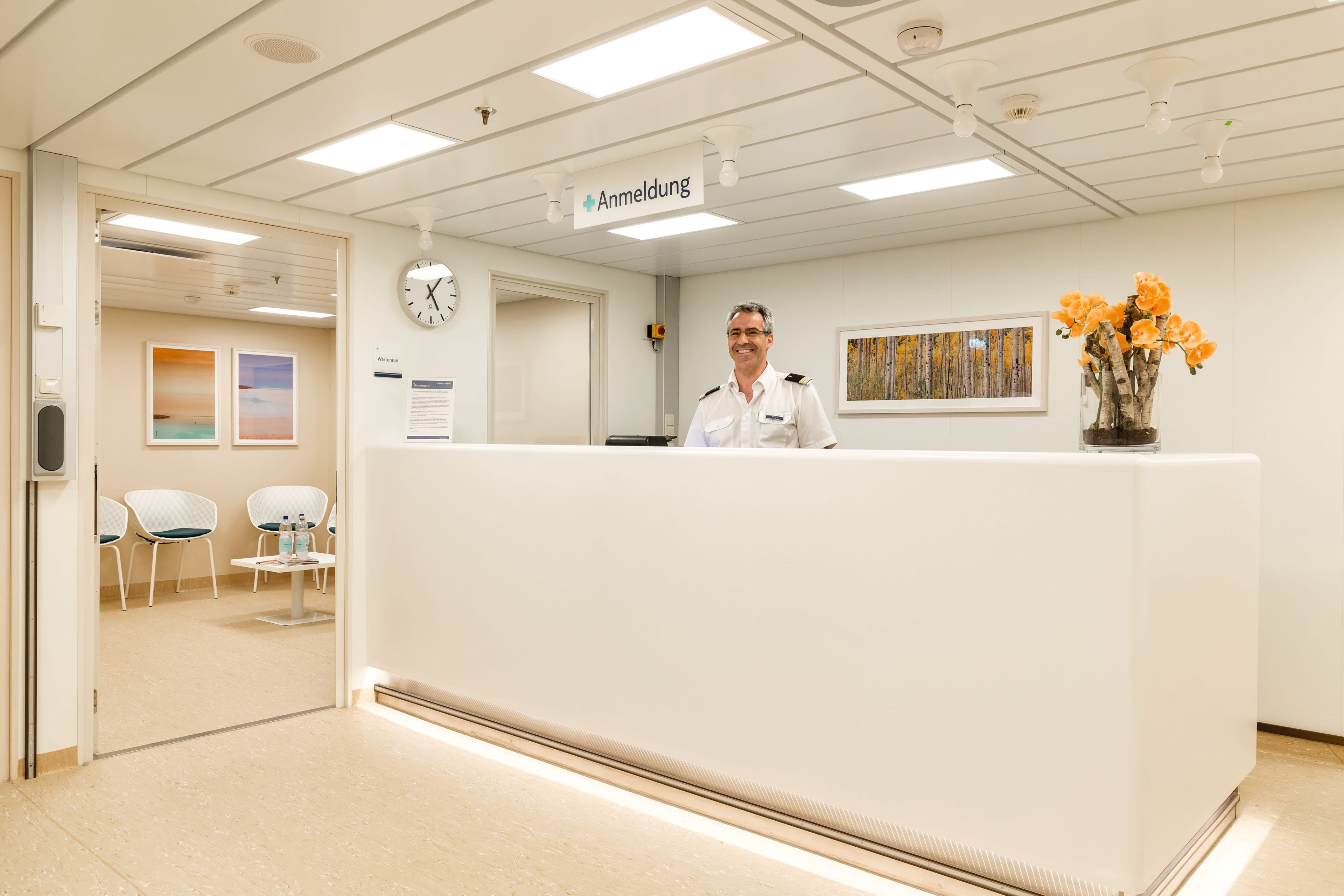Mann in Uniform an Rezeption, Kreuzfahrtschiff, helle Einrichtung, Blumen.