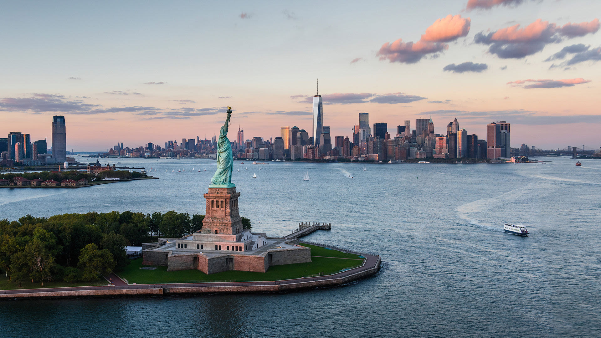 Freiheitsstatue vor New York Skyline bei Sonnenuntergang.