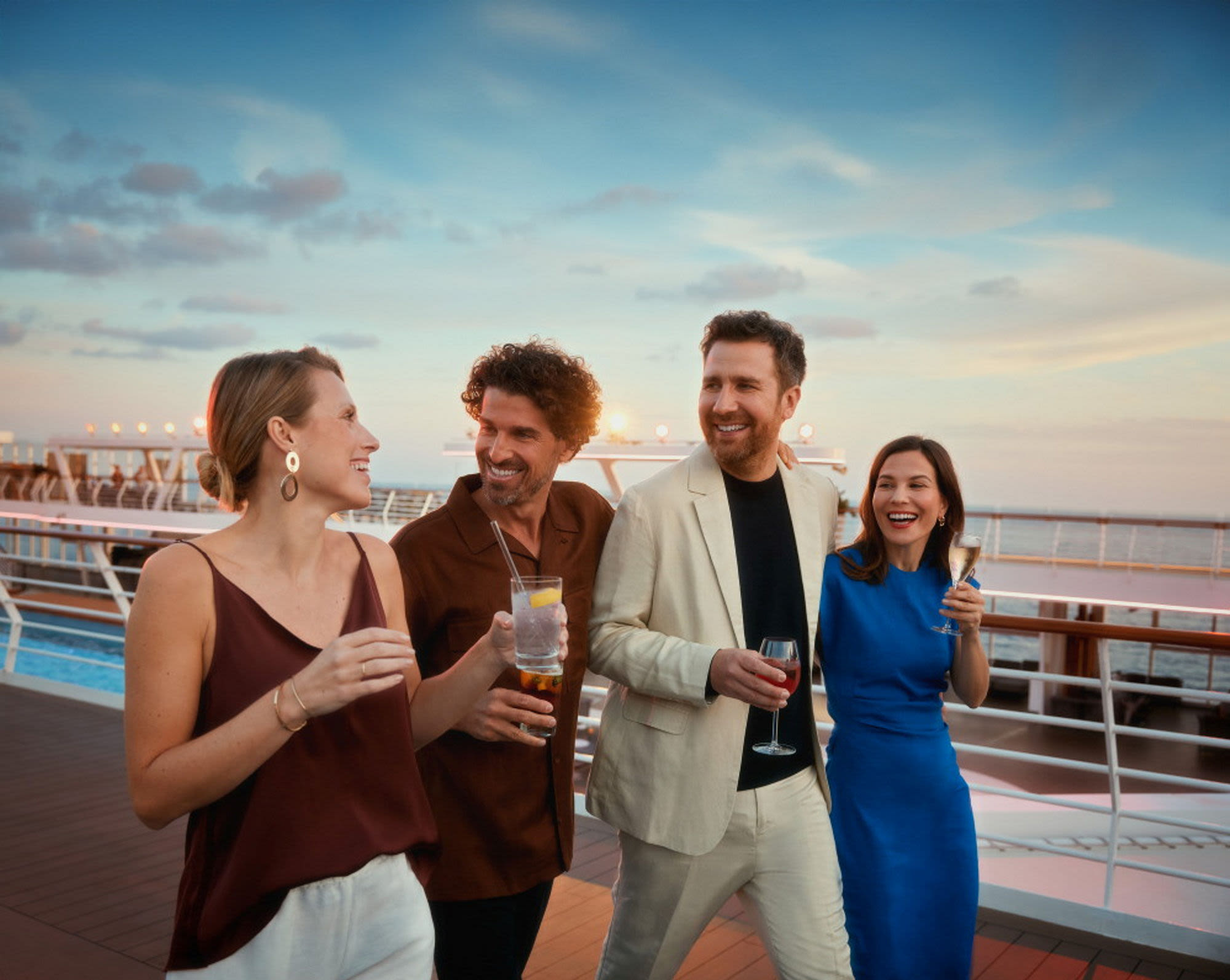 Vier Personen lachen auf einem Kreuzfahrtschiff der Mein Schiff® Flotte bei Sonnenuntergang.