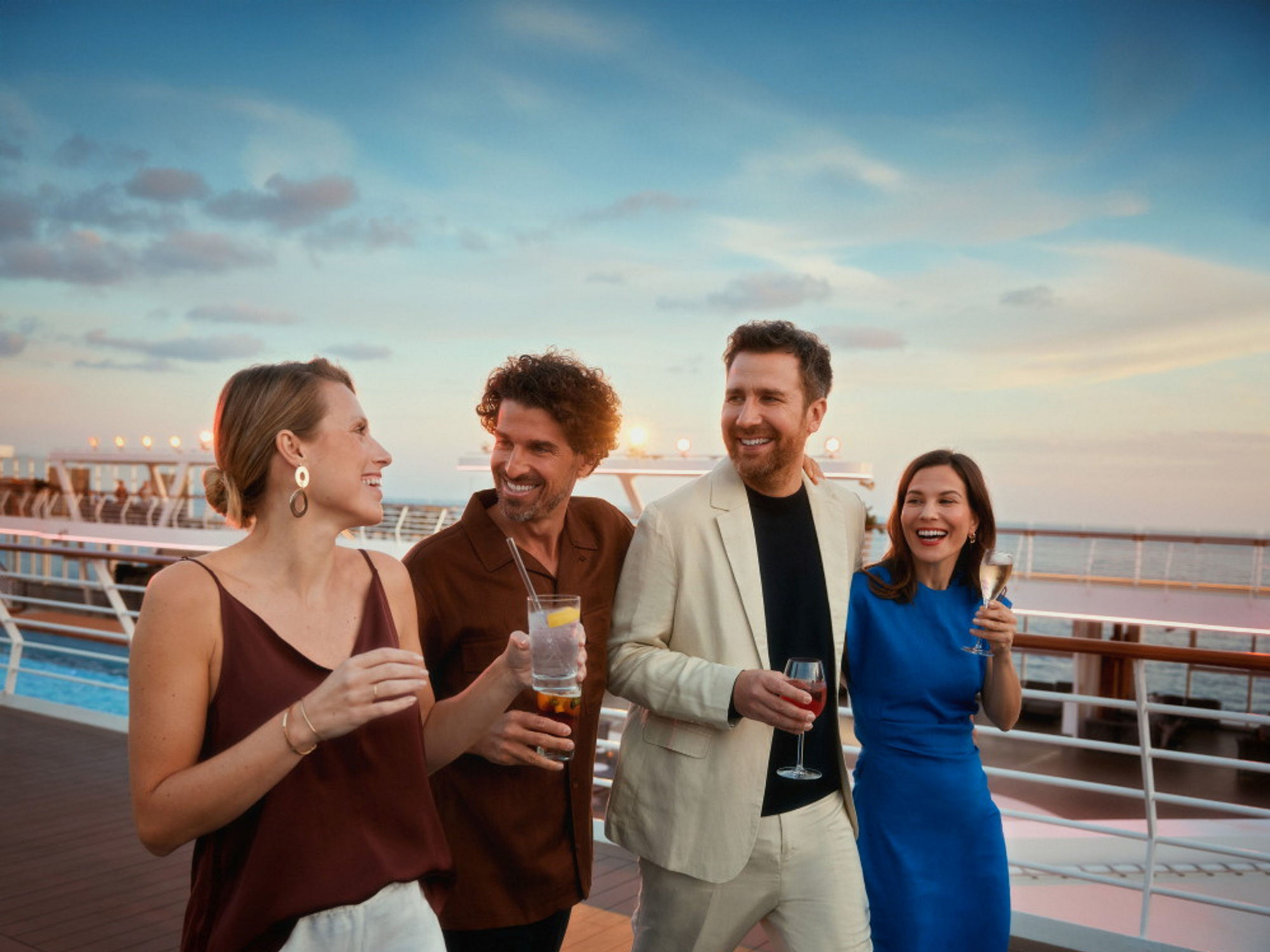 Adults only Vier Personen lachen auf einem Kreuzfahrtschiff der Mein Schiff® Flotte bei Sonnenuntergang.