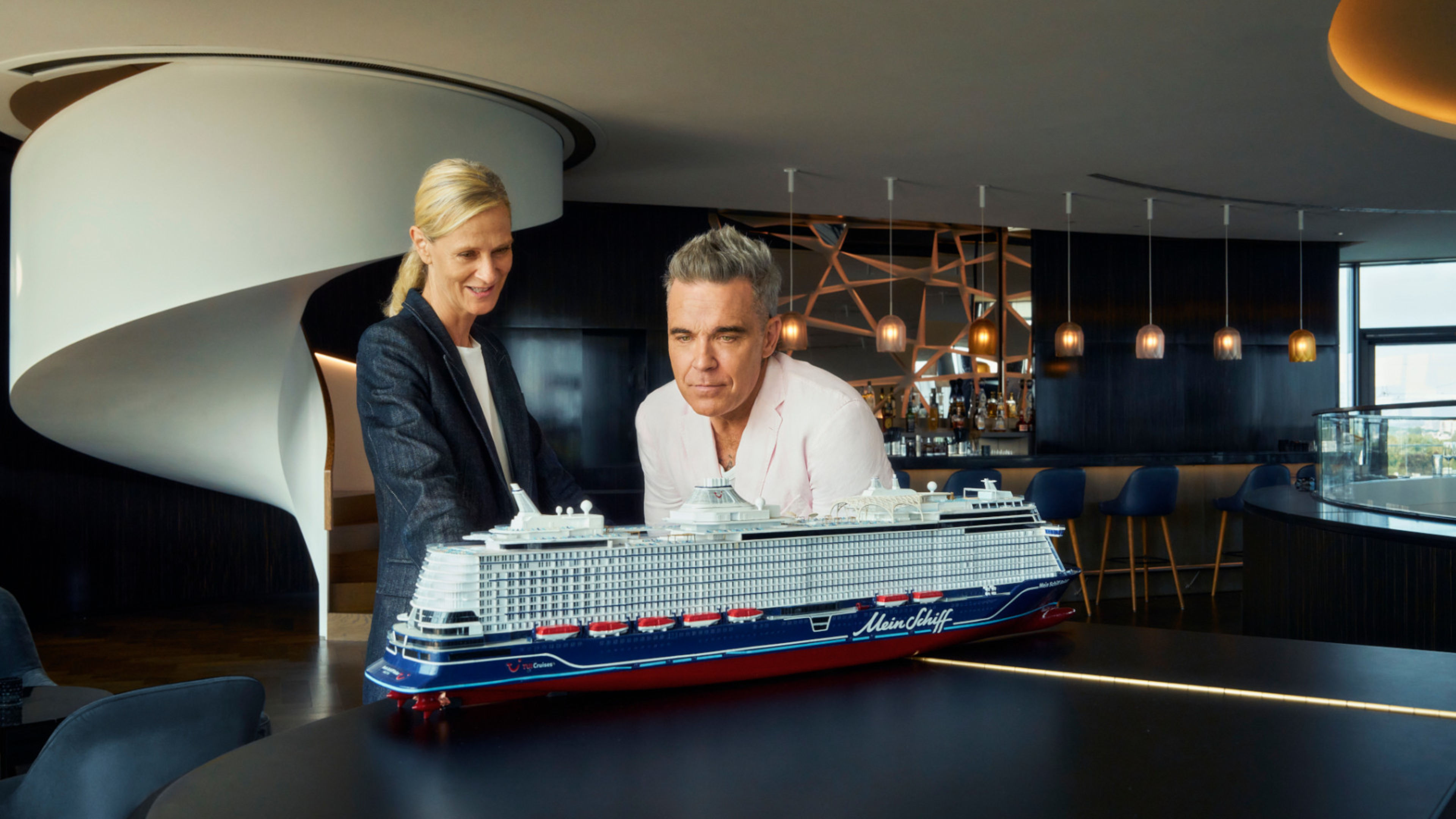 Zwei Personen betrachten Modell eines Kreuzfahrtschiffs der Mein Schiff® Flotte in modernem Raum. Zwei Personen betrachten Modell eines Kreuzfahrtschiffs der Mein Schiff® Flotte in modernem Raum.