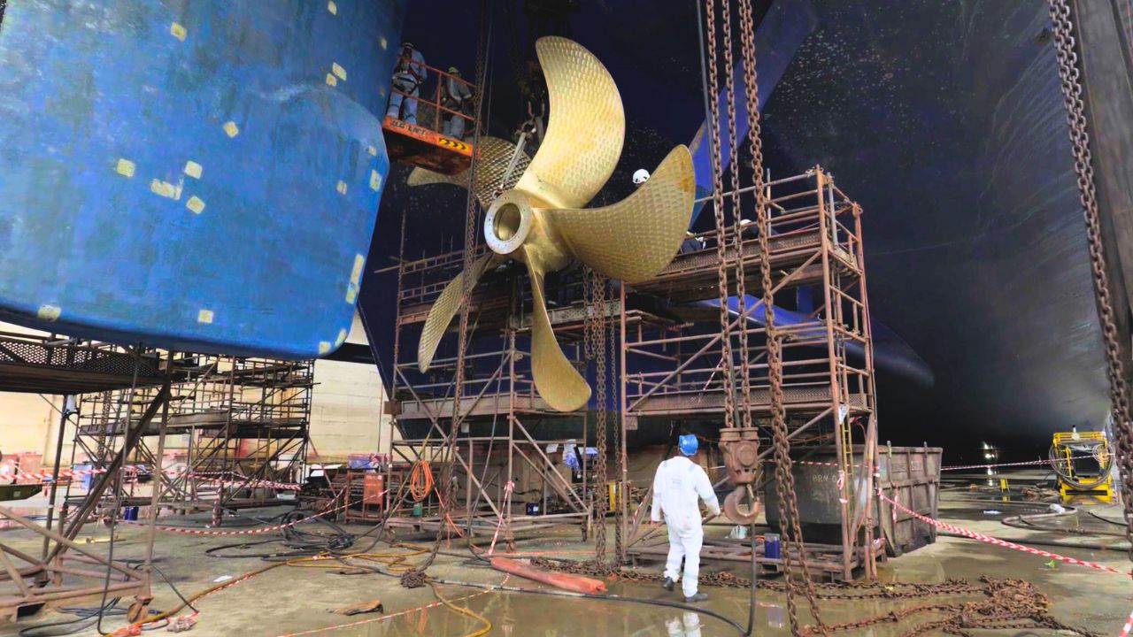 Arbeiter im Trockendock reparieren Schiffsschraube, Gerüste, blaue Schiffswand.