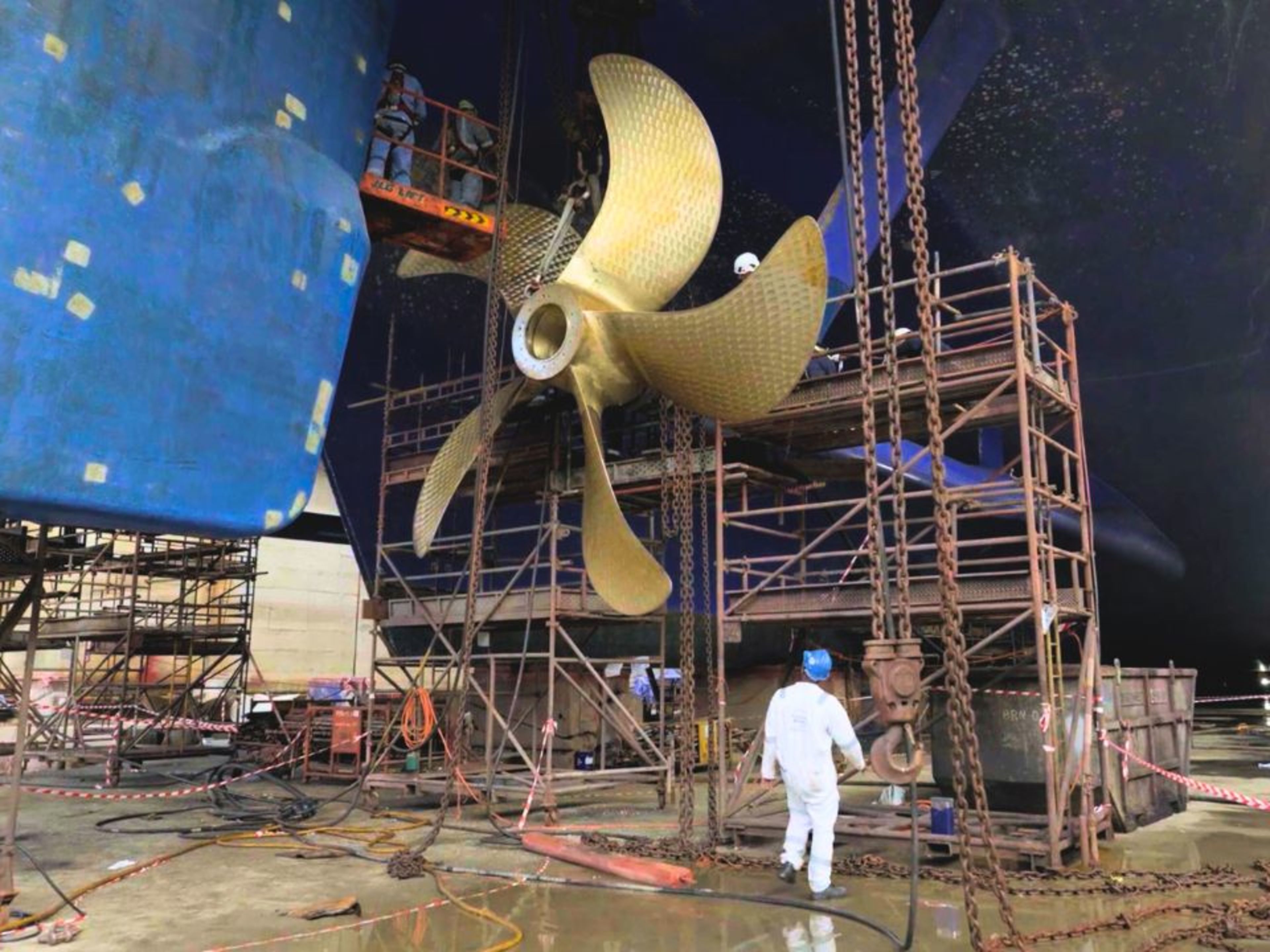 Propellerwechsel Mein Schiff 4 Arbeiter im Trockendock reparieren Schiffsschraube, Gerüste, blaue Schiffswand.