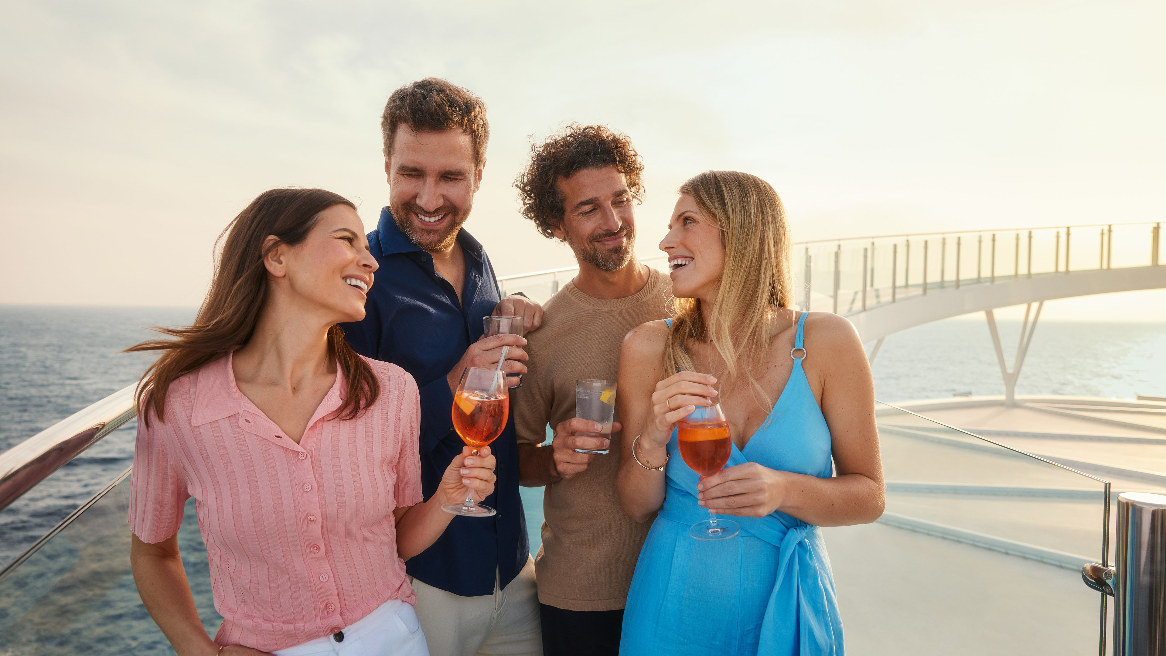 Vier Personen genießen Getränke auf einem Kreuzfahrtschiff der Mein Schiff® Flotte bei Sonnenuntergang.