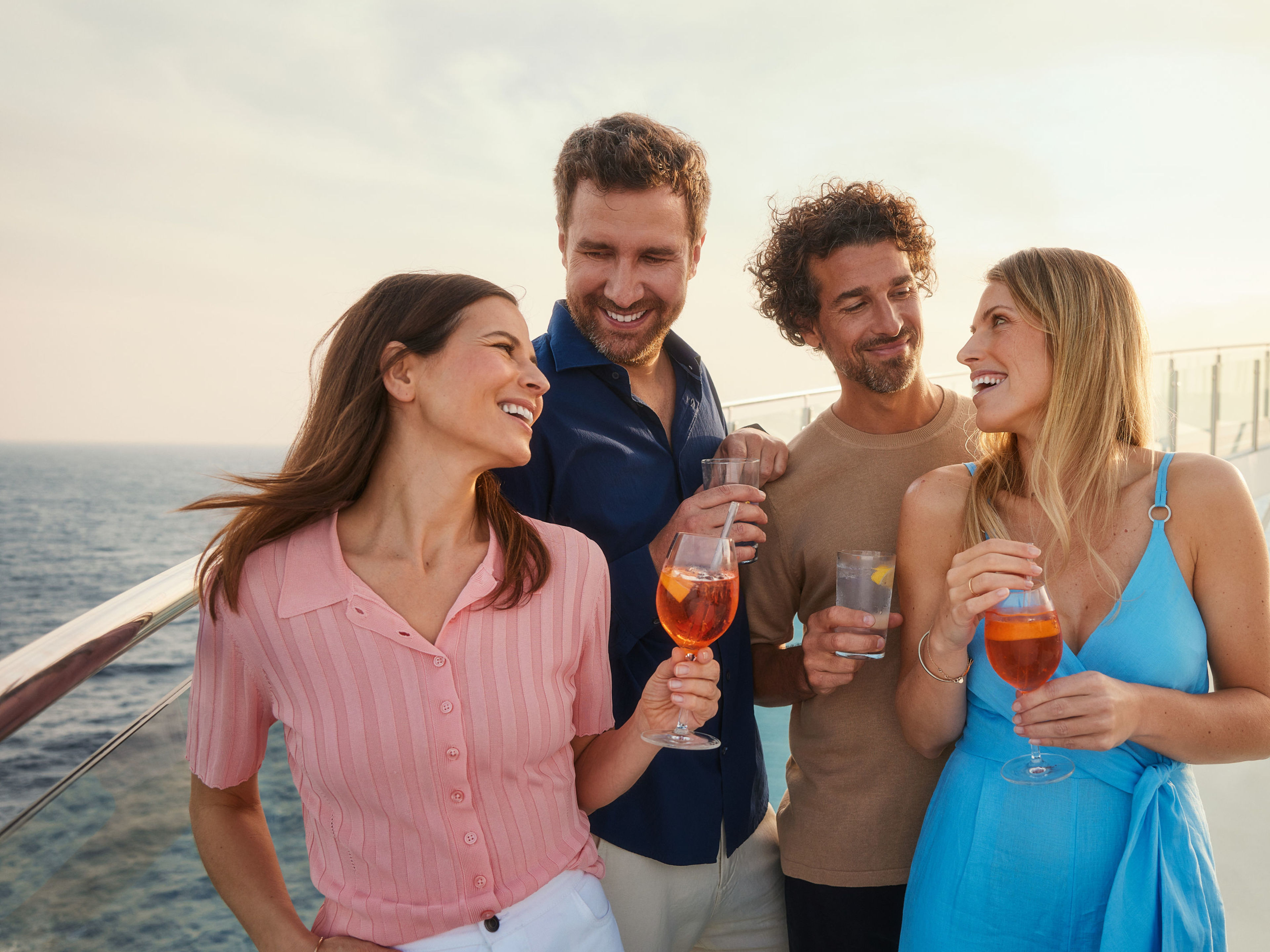 Mit Freunden genießen Vier Personen genießen Getränke auf einem Kreuzfahrtschiff der Mein Schiff® Flotte bei Sonnenuntergang.