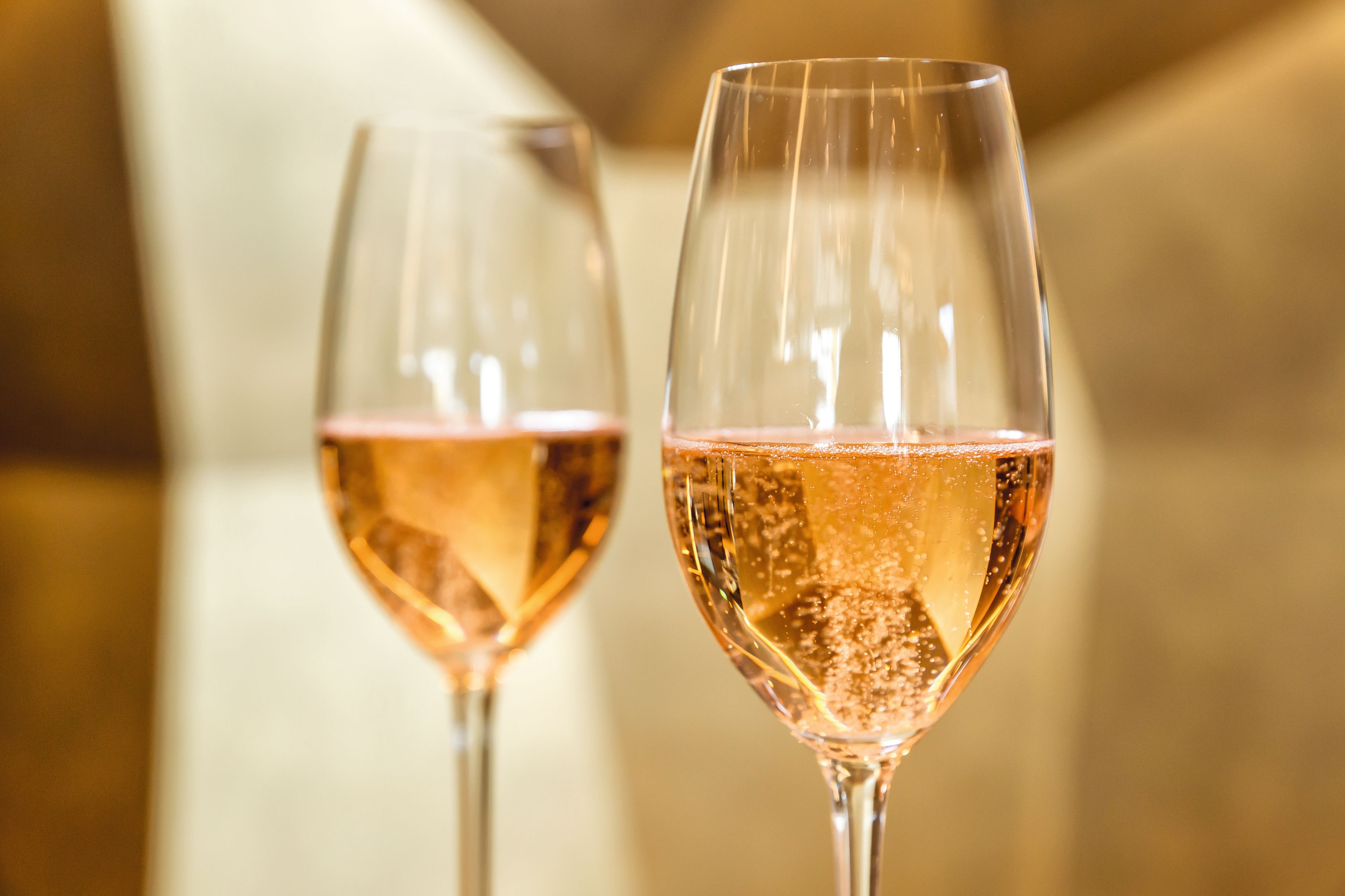 Zwei Gläser Rosé-Sekt mit goldener Hintergrundbeleuchtung.