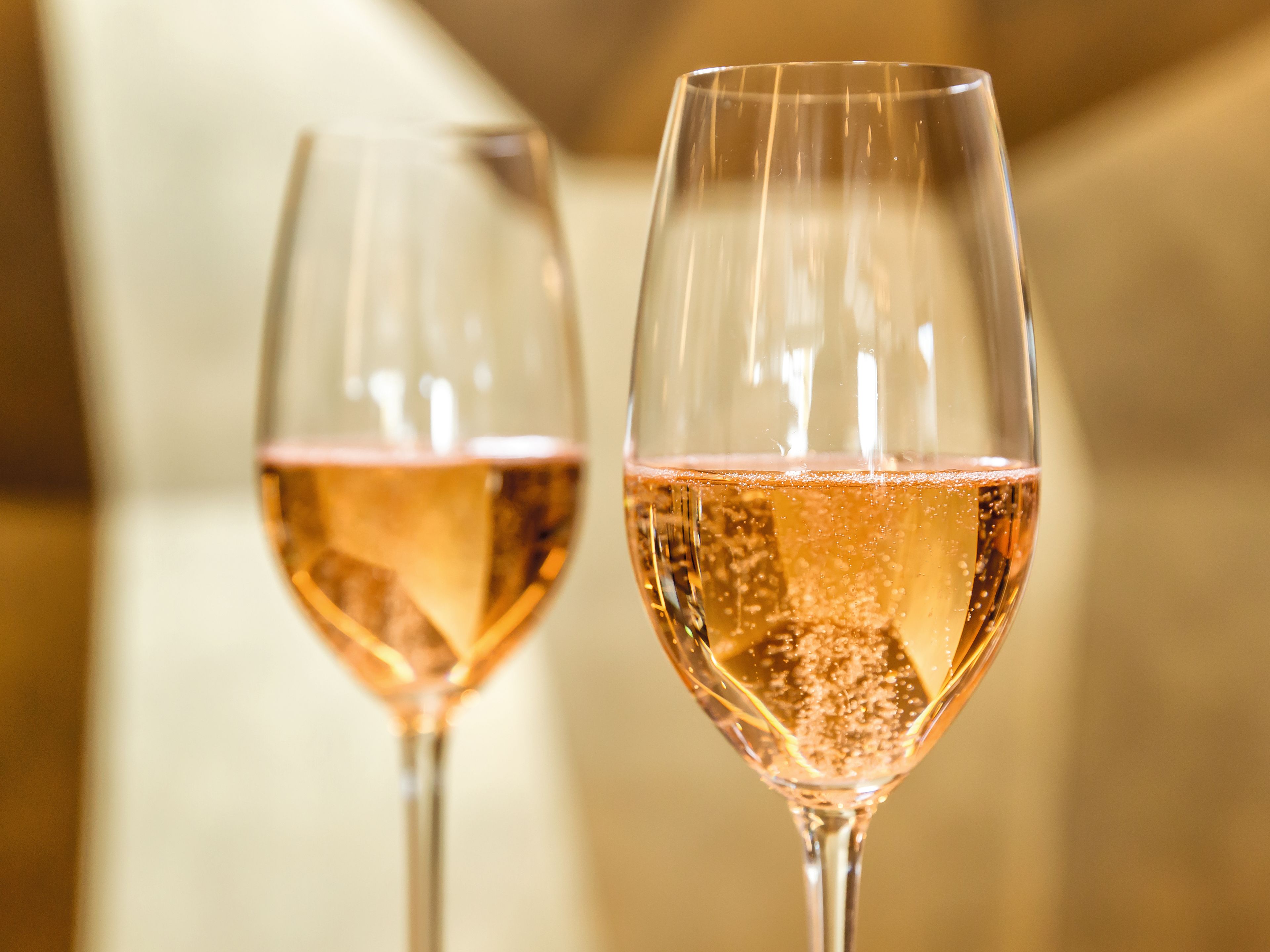 Zwei Gläser Rosé-Sekt mit goldener Hintergrundbeleuchtung. Zwei Gläser Rosé-Sekt mit goldener Hintergrundbeleuchtung.