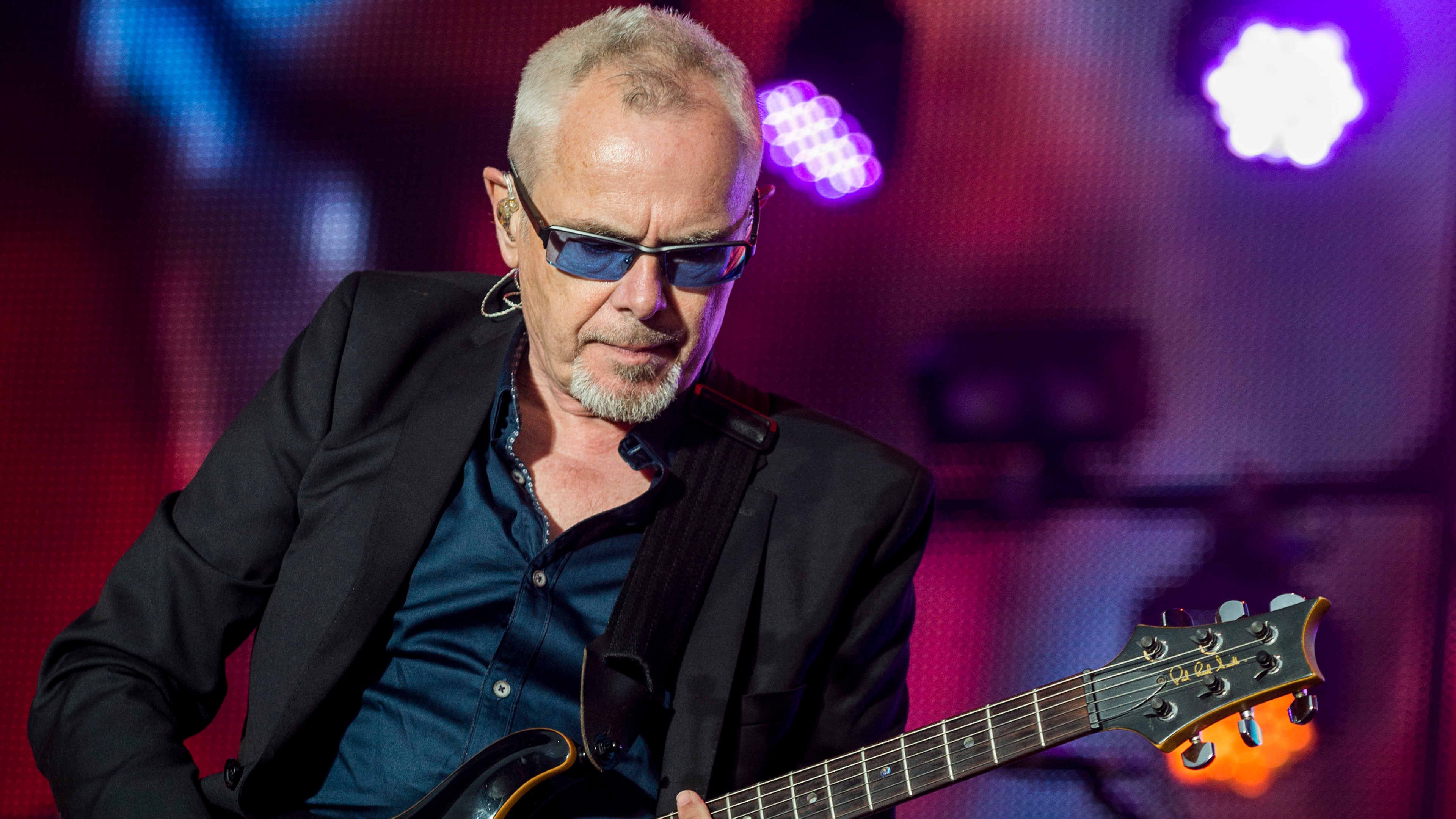 Mann mit Sonnenbrille spielt E-Gitarre auf Bühne.