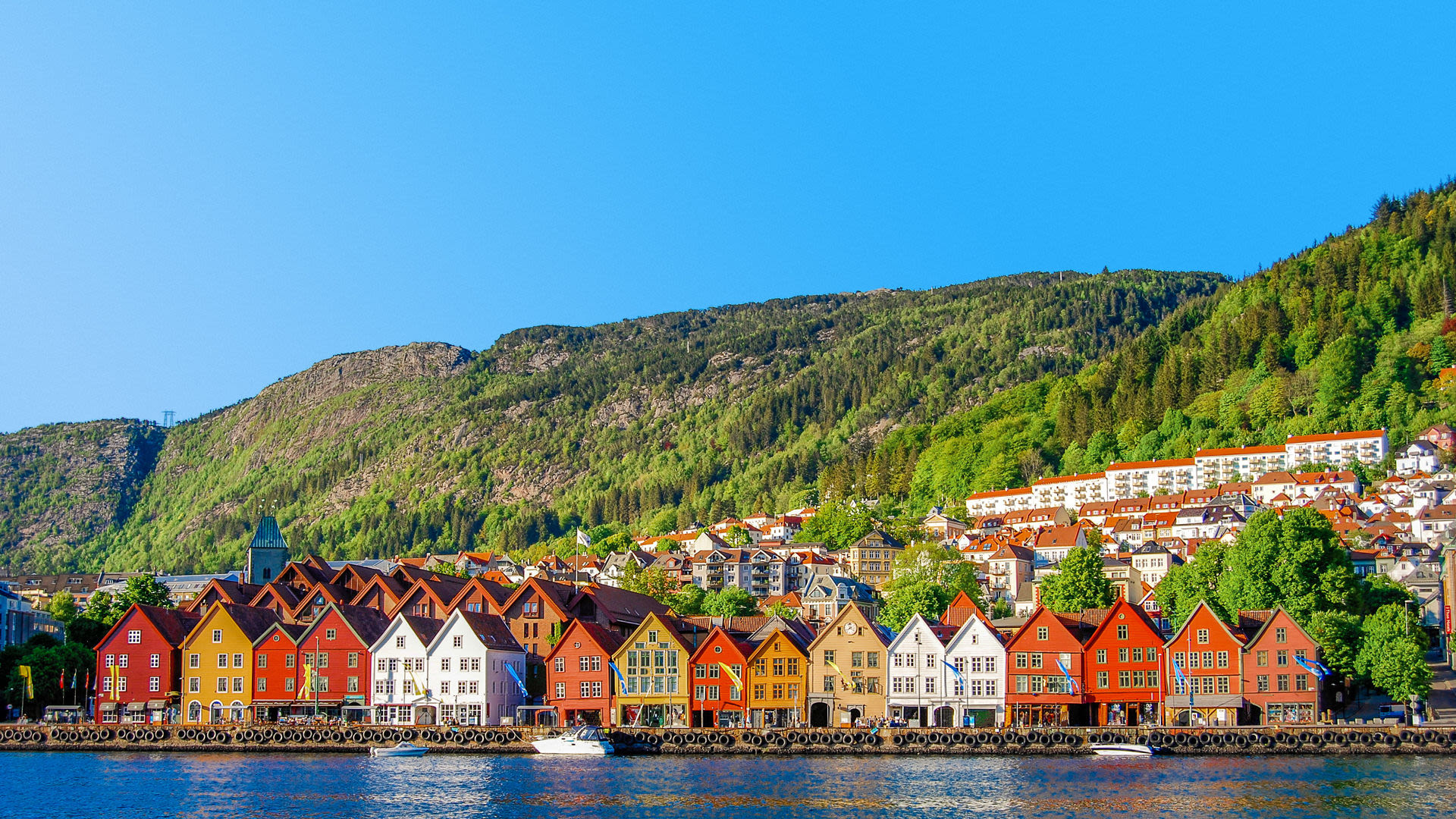 Bunte Holzhäuser am Wasser in Bergen, Norwegen, vor grünen Hügeln. Bunte Holzhäuser am Wasser in Bergen, Norwegen, vor grünen Hügeln.