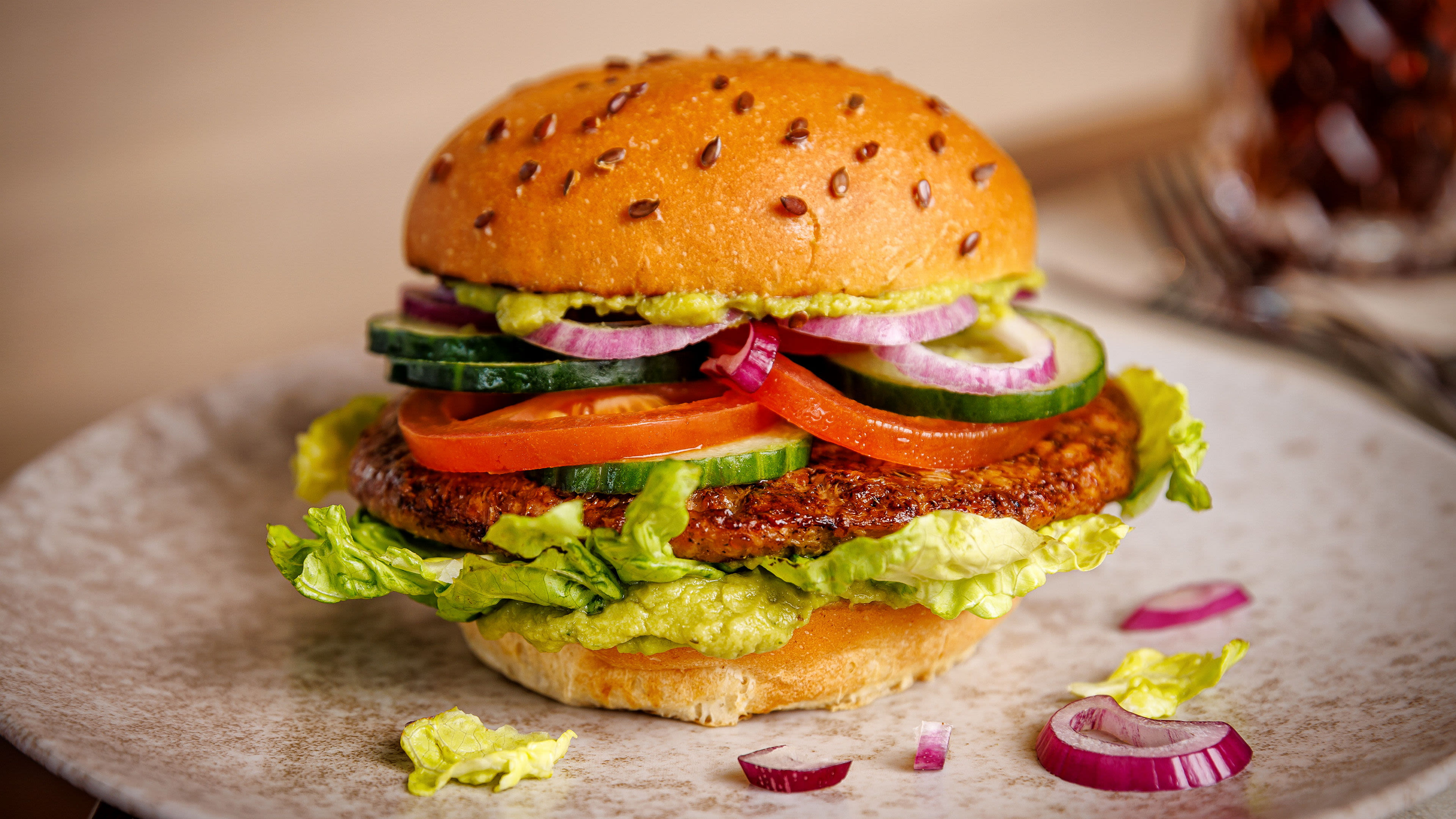 Veggie-Burger mit Salat, Tomaten, Gurken und roten Zwiebeln auf einem Teller.