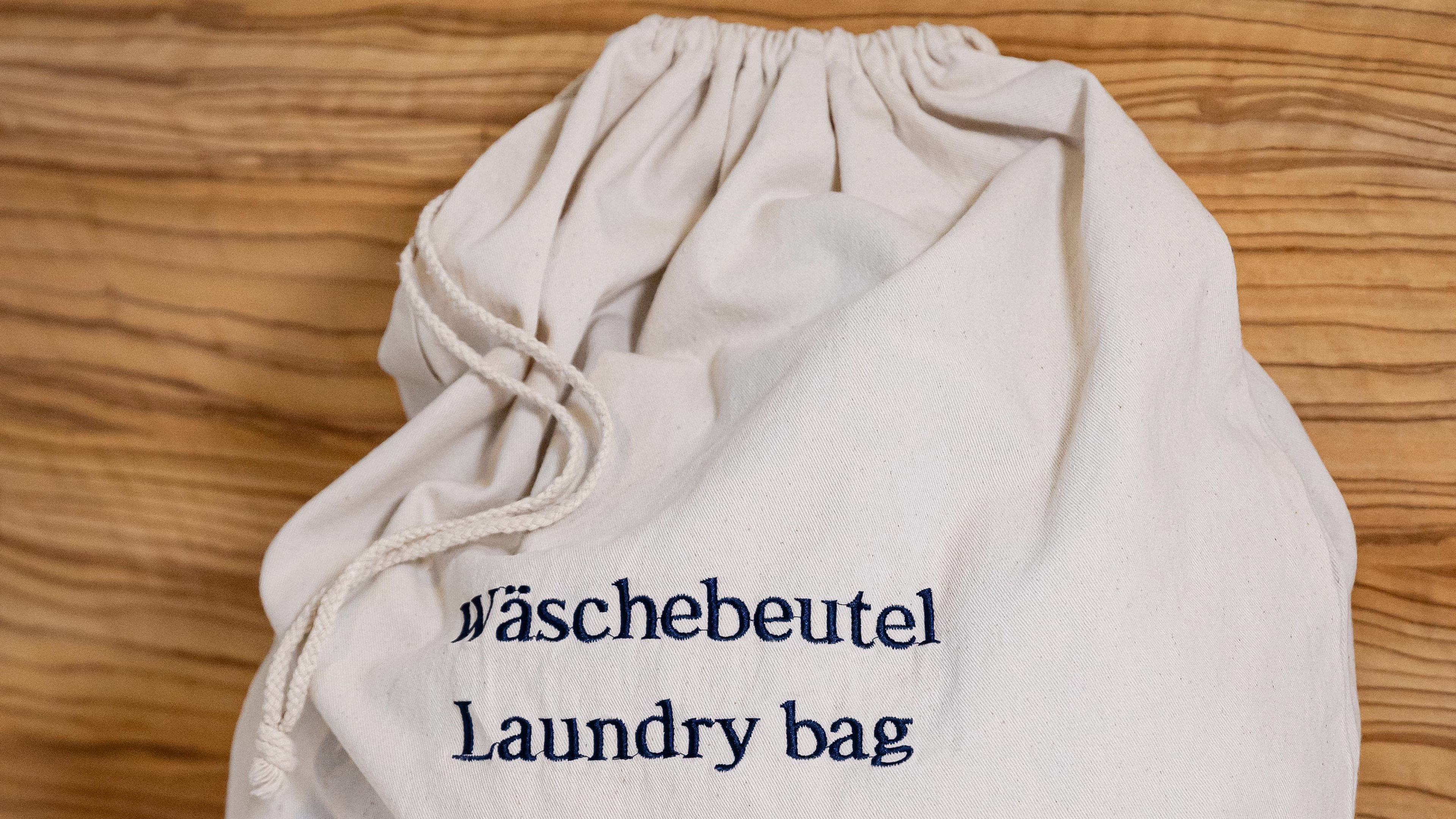 Beiger Wäschebeutel mit blauer Aufschrift auf Holzhintergrund.