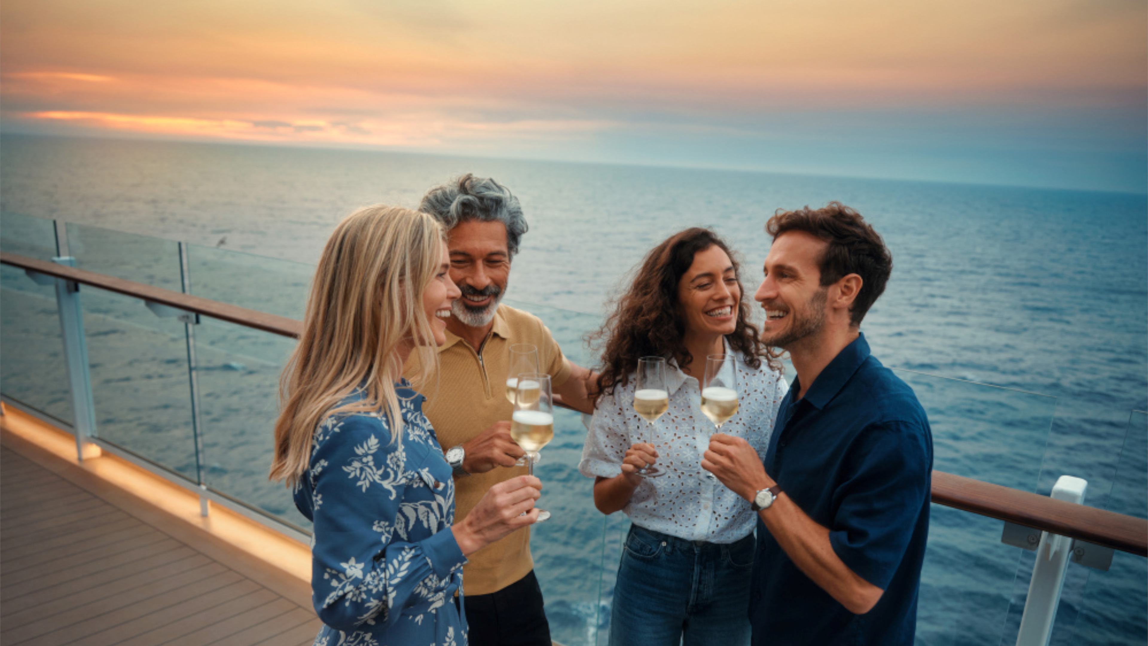 Vier Personen stoßen mit Sekt auf einem Kreuzfahrtschiff bei Sonnenuntergang an.