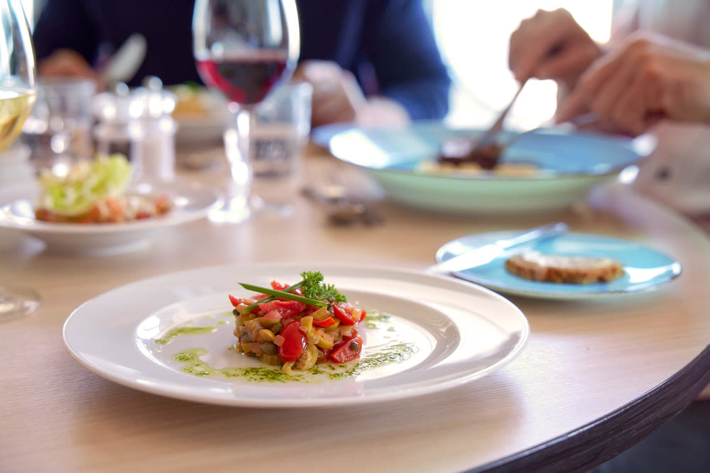 Gourmetgericht auf weißem Teller, Glas Rotwein, gedeckter Tisch.