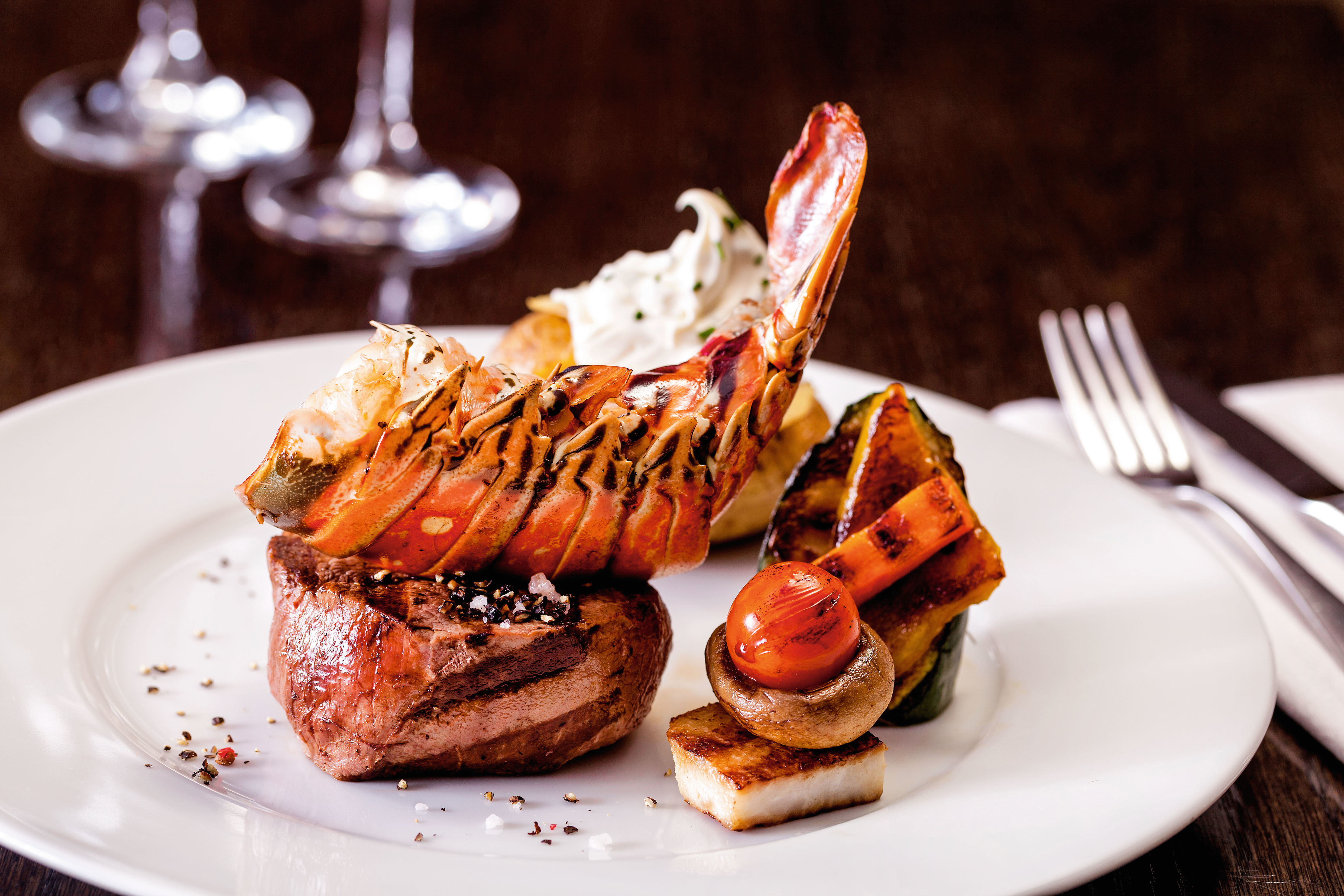 Hummer und Steak auf weißem Teller mit Gemüse.