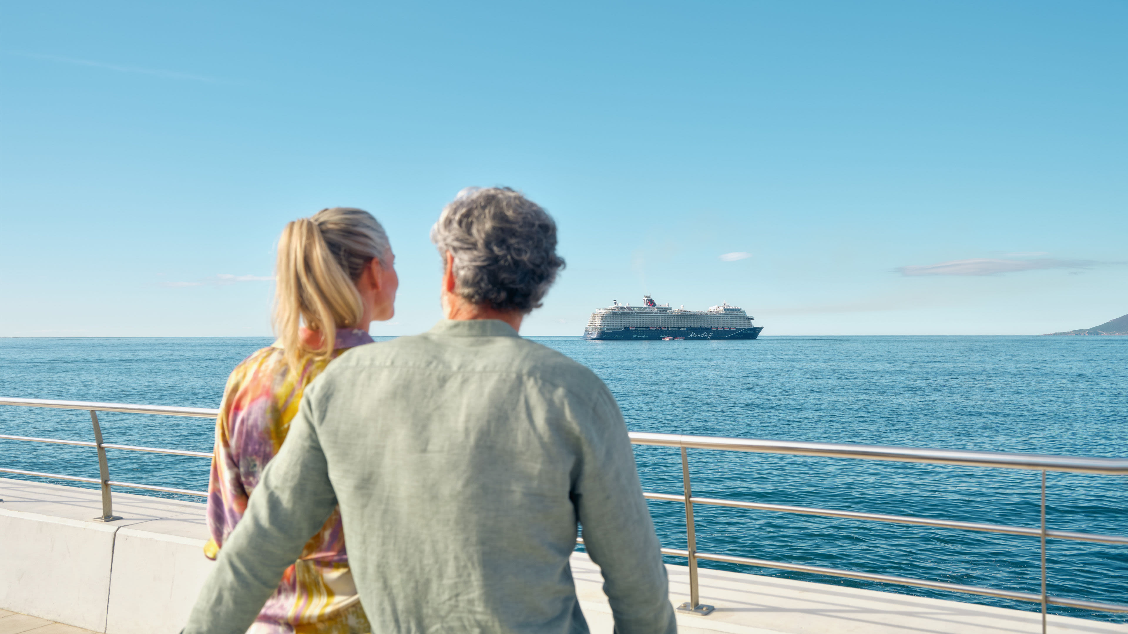 Paar blickt auf Kreuzfahrtschiff der Mein Schiff® Flotte im Meer.