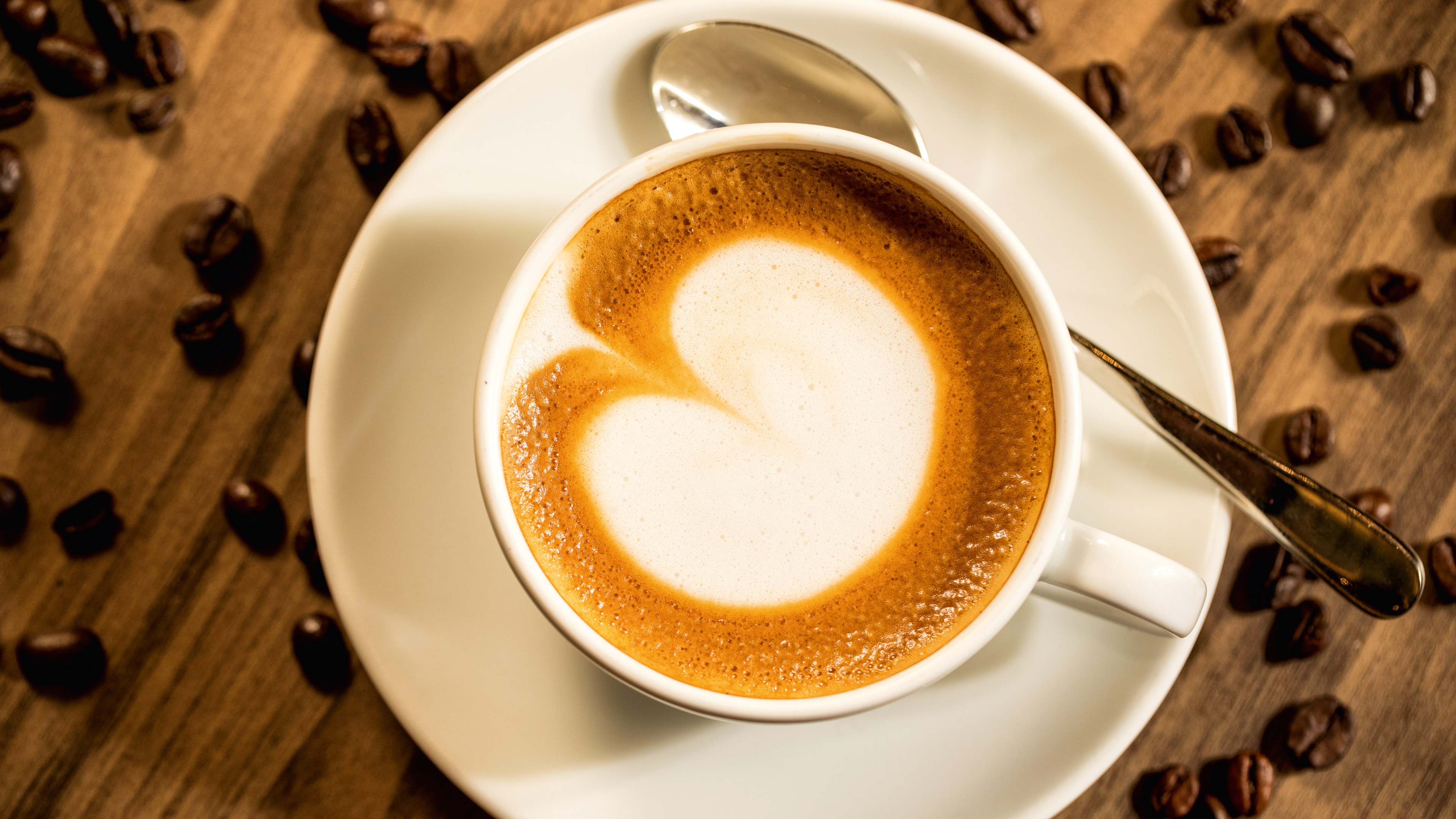 Cappuccino mit Herzmuster, Kaffeebohnen auf Holztisch.