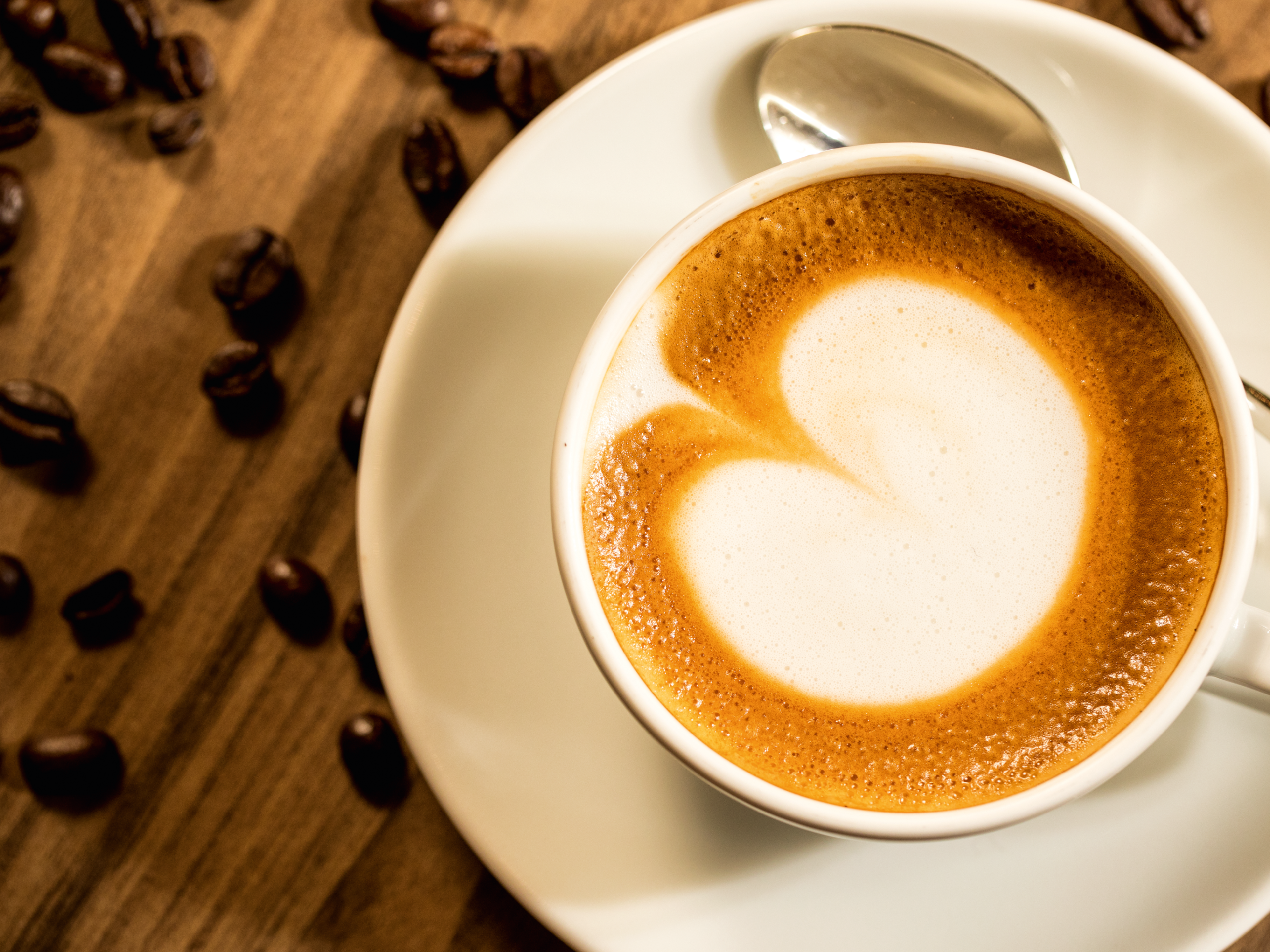 Nachhaltigkeit - Kaffeetasse Original Beans Cappuccino mit Herzmuster, Kaffeebohnen auf Holztisch.