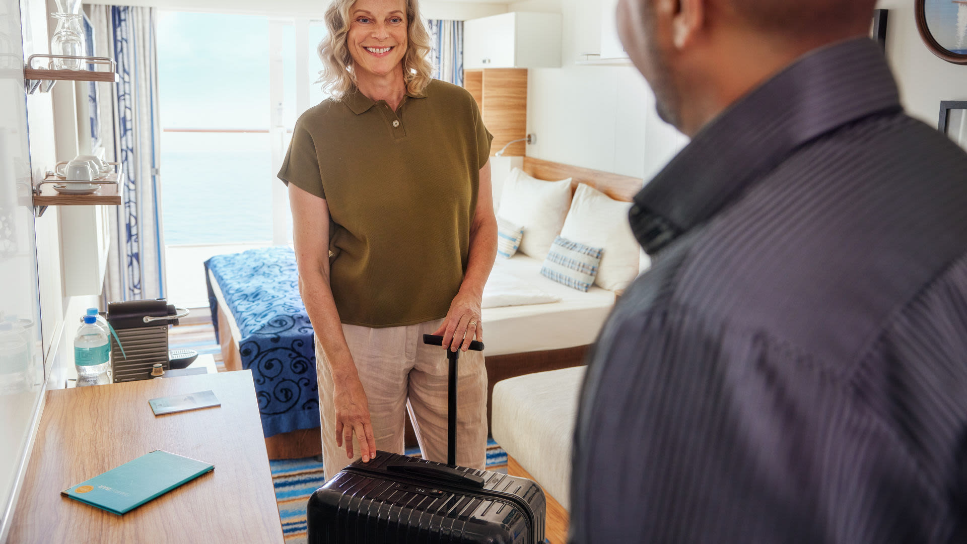 Frau mit Koffer in Kreuzfahrtschiff-Kabine, lächelnd, Meerblick.