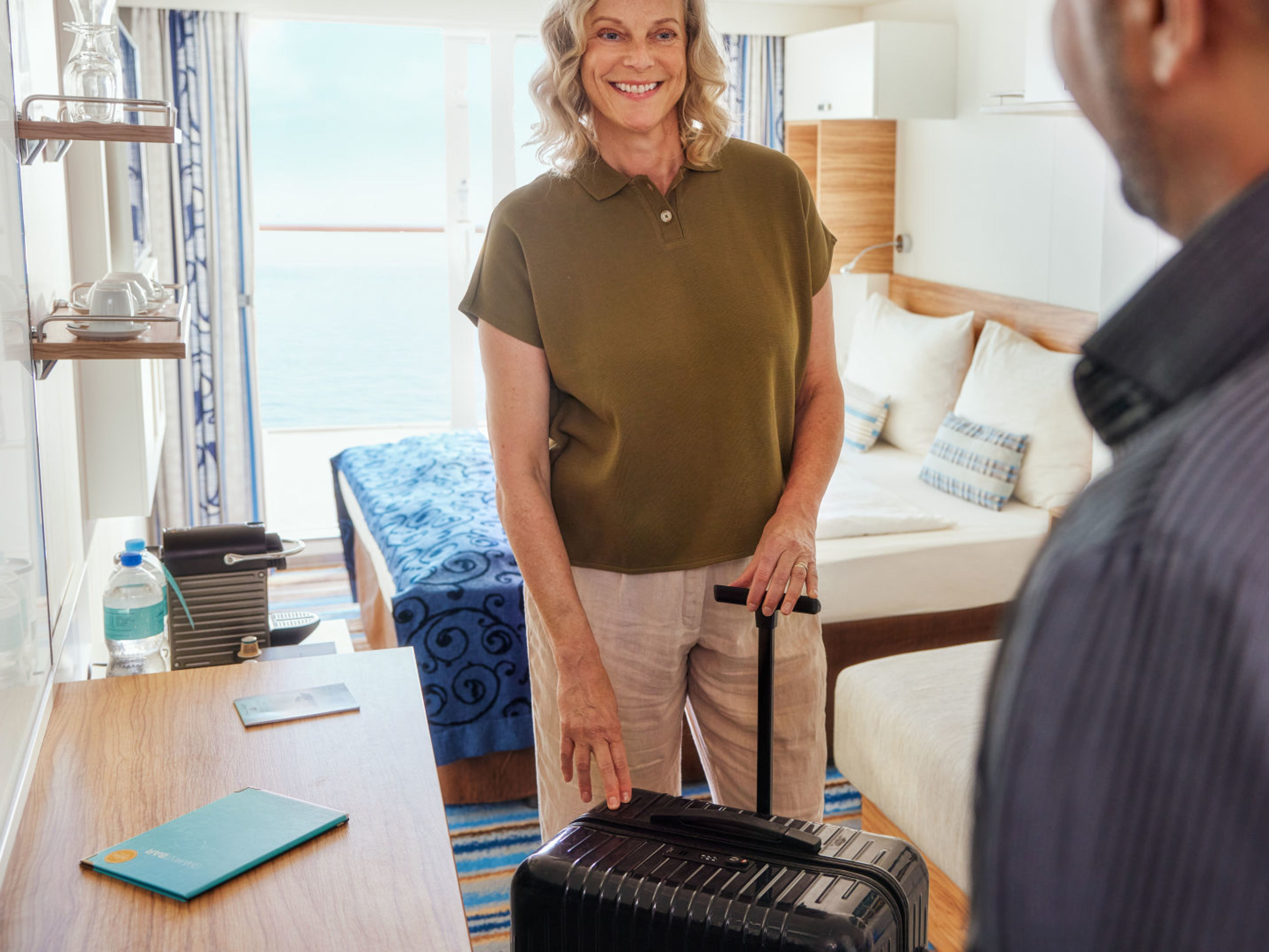 Frau nimmt Koffer auf Kabine in Empfang Frau mit Koffer in Kreuzfahrtschiff-Kabine, lächelnd, Meerblick.