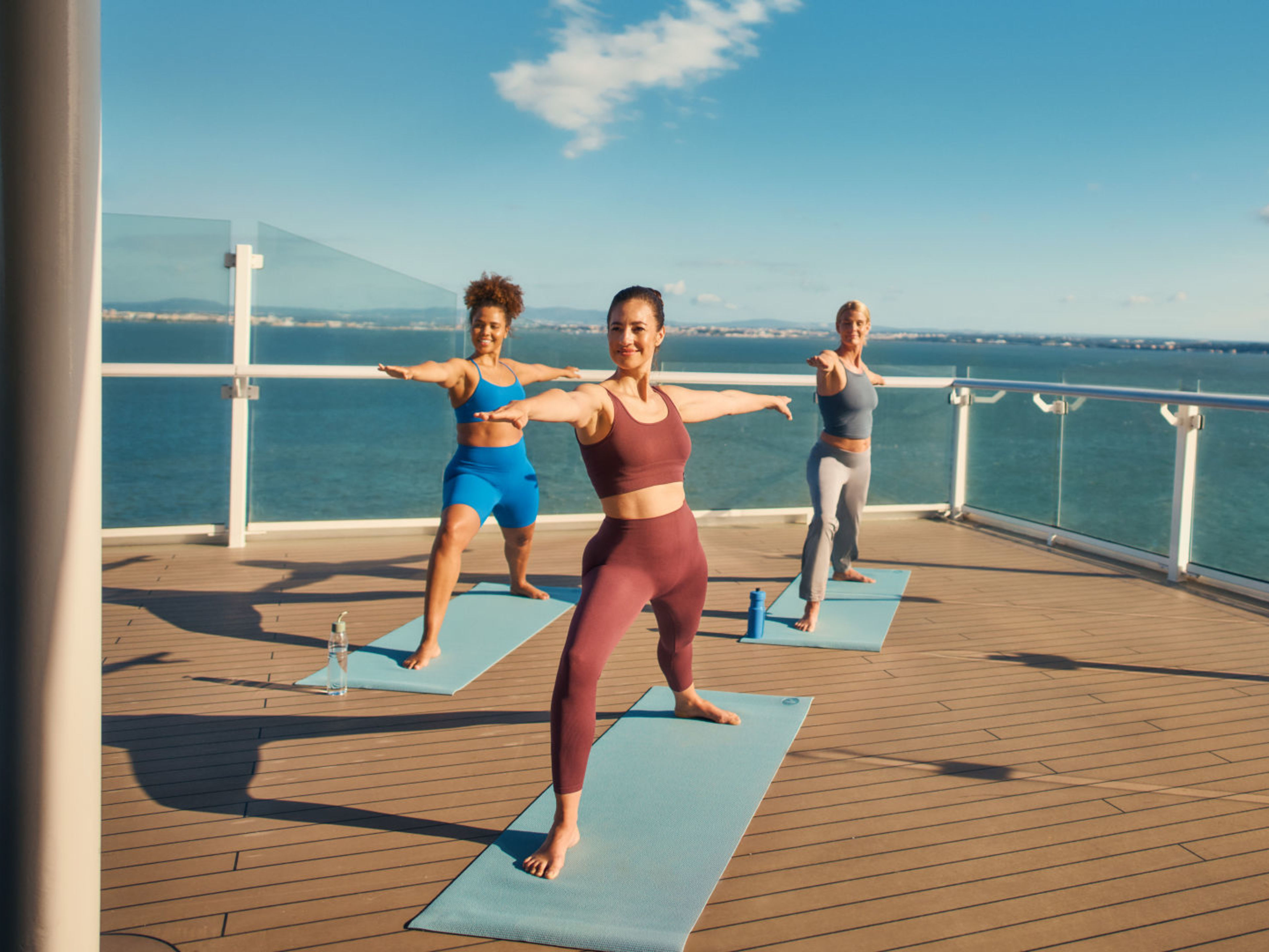 Drei Freundinnen machen gemeinsam Yoga in der Sonne an Deck Drei Frauen machen Yoga auf einem Kreuzfahrtschiffdeck.