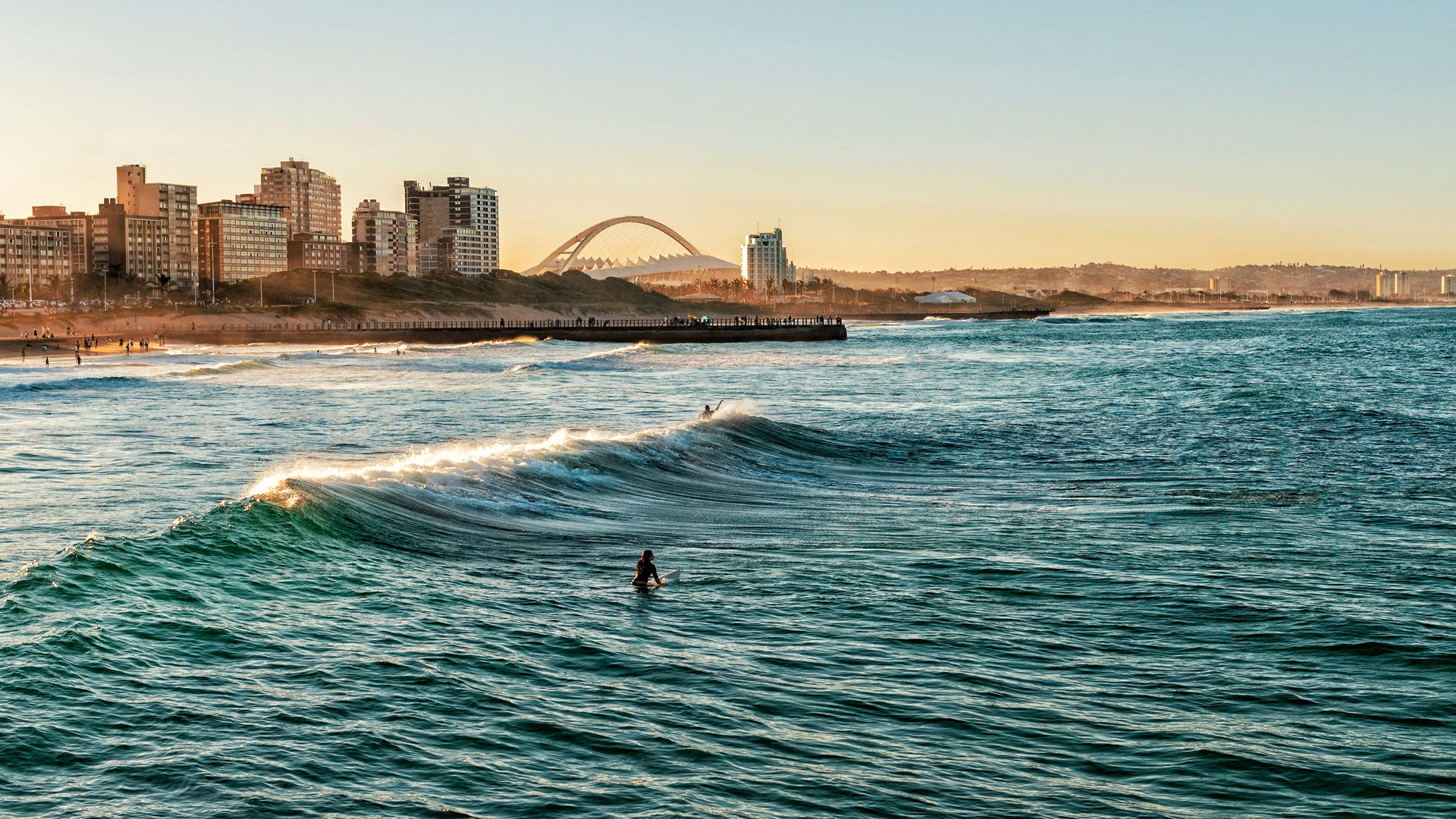 Surfer auf Wellen vor Durban Skyline bei Sonnenuntergang.