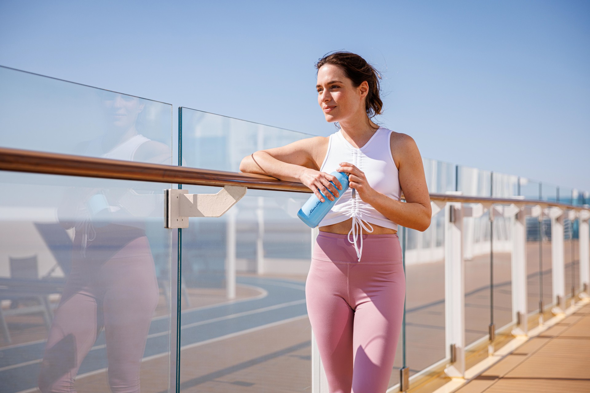 Frau in Sportkleidung mit Wasserflasche auf Kreuzfahrtschiff-Deck.