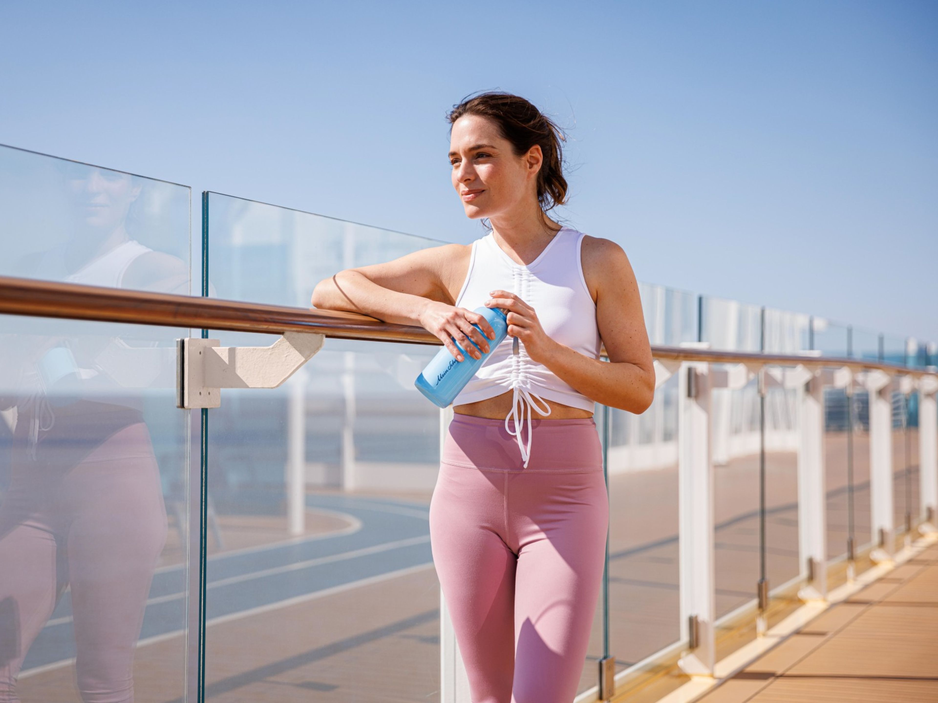 Fan Kollektion Mein Schiff Fanshop Frau in Sportkleidung mit Wasserflasche auf Kreuzfahrtschiff-Deck.