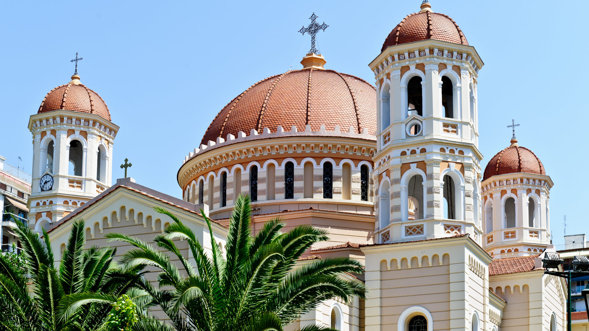 Kirche mit roten Kuppeln und Palmen, blauer Himmel.