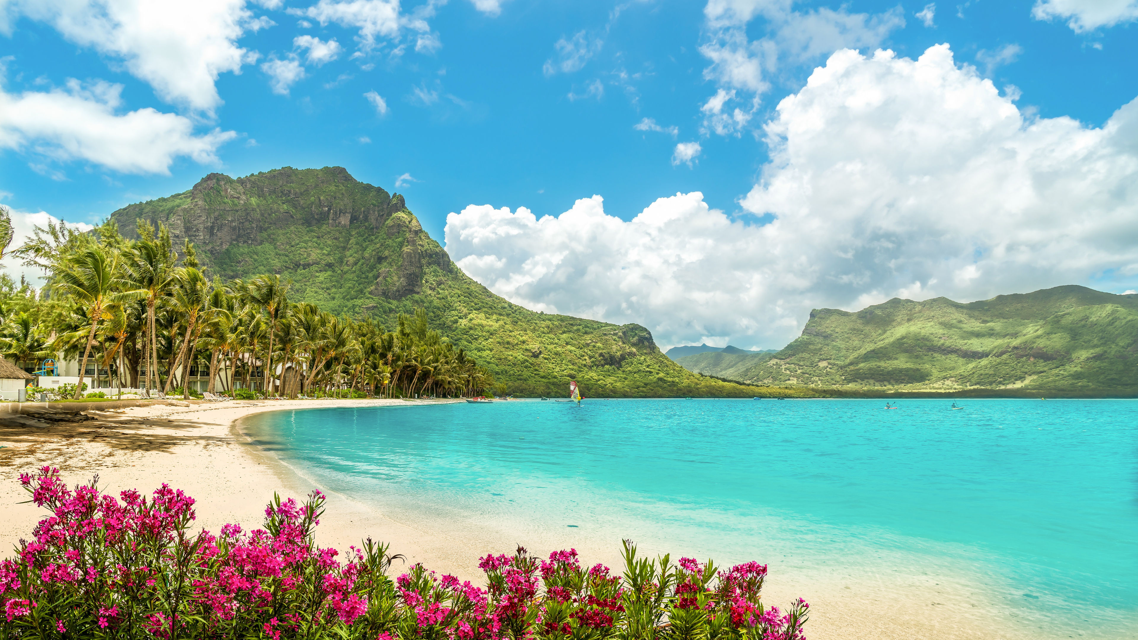 Tropischer Strand mit Palmen, türkisfarbenem Wasser und grünen Bergen.