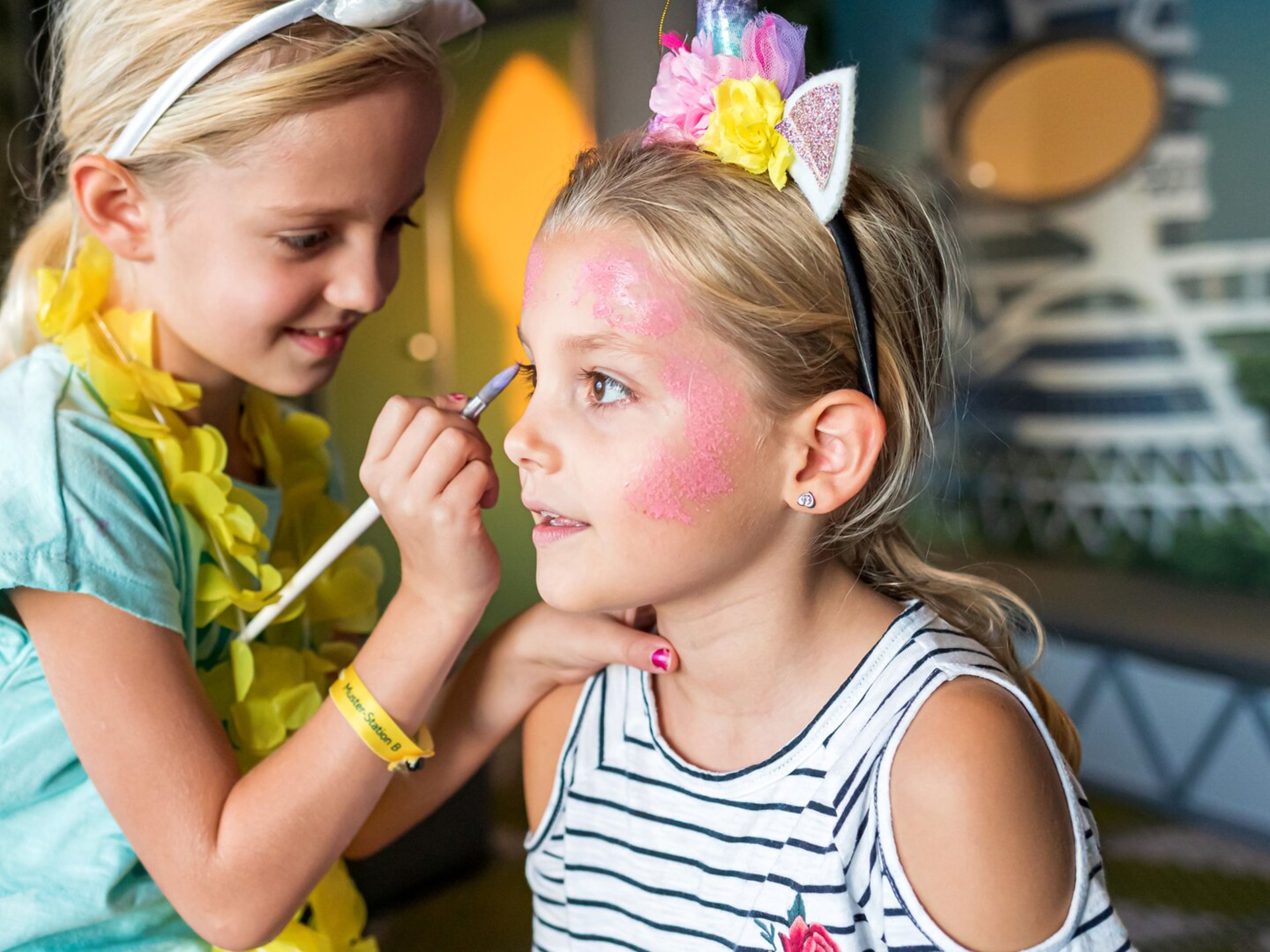 Kinderschminken Ostern Mädchen schminkt ein anderes mit rosa Farbe, lächelnd.