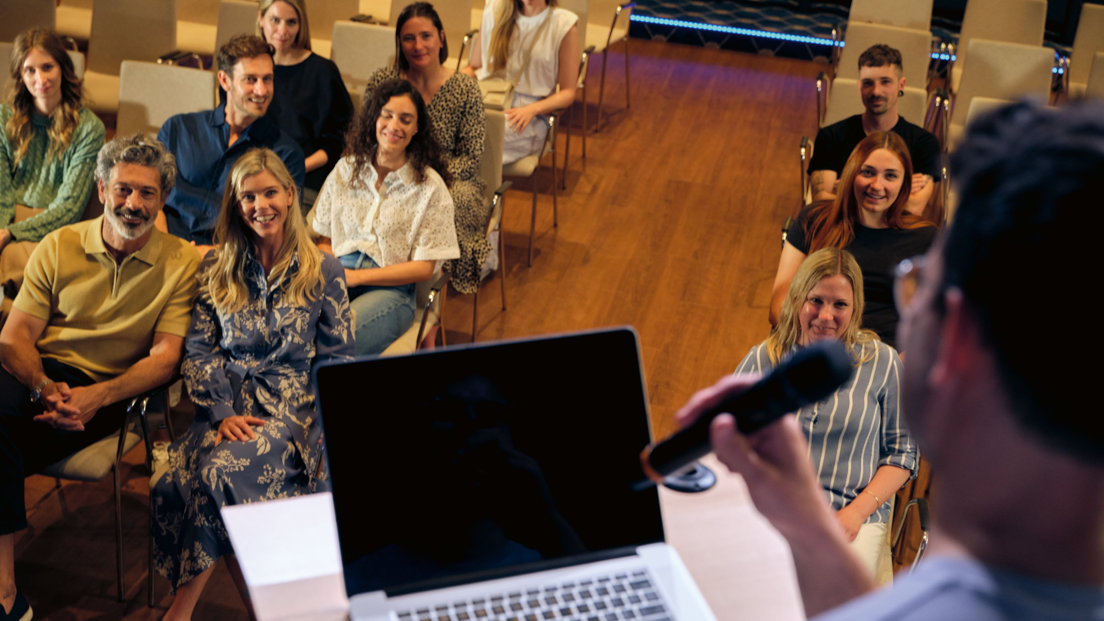 Person spricht vor lächelndem Publikum in einem Konferenzraum.