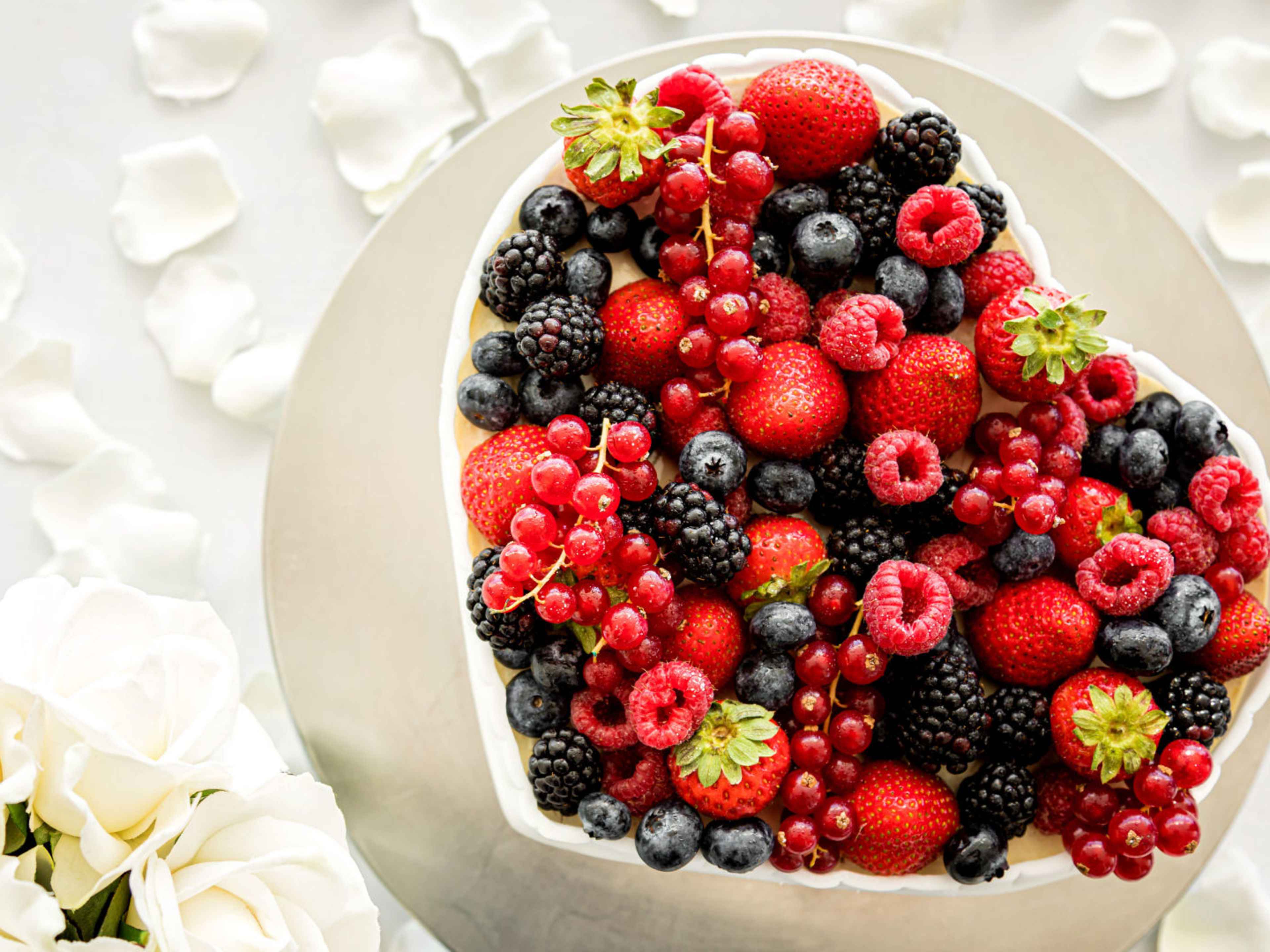 Torte Herzförmige Beeren-Torte mit weißen Rosen und Blütenblättern.