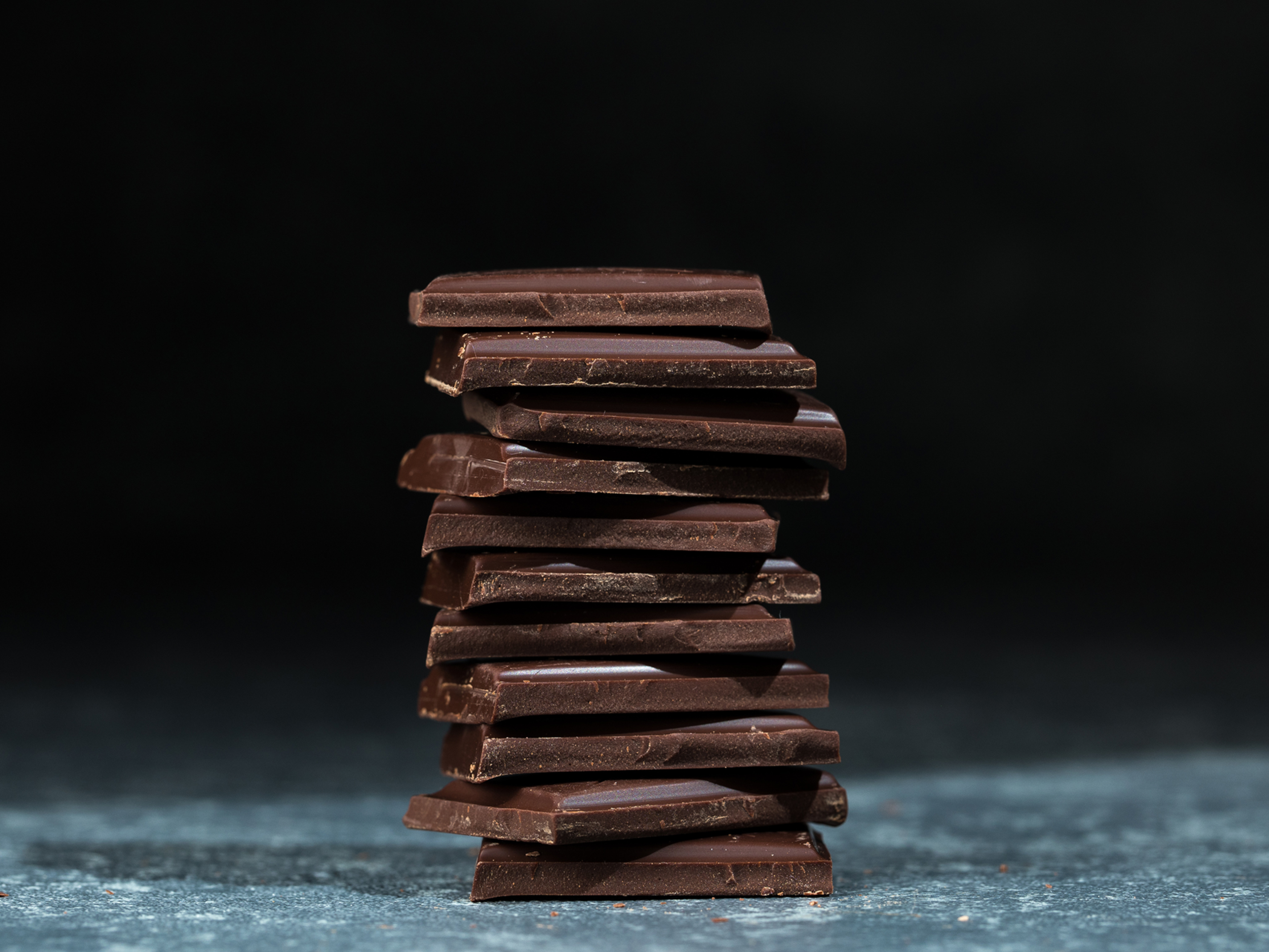 Nachhaltigkeit - Original Beans - Chocolate Tower Stapel dunkler Schokoladenstücke auf grauem Untergrund.