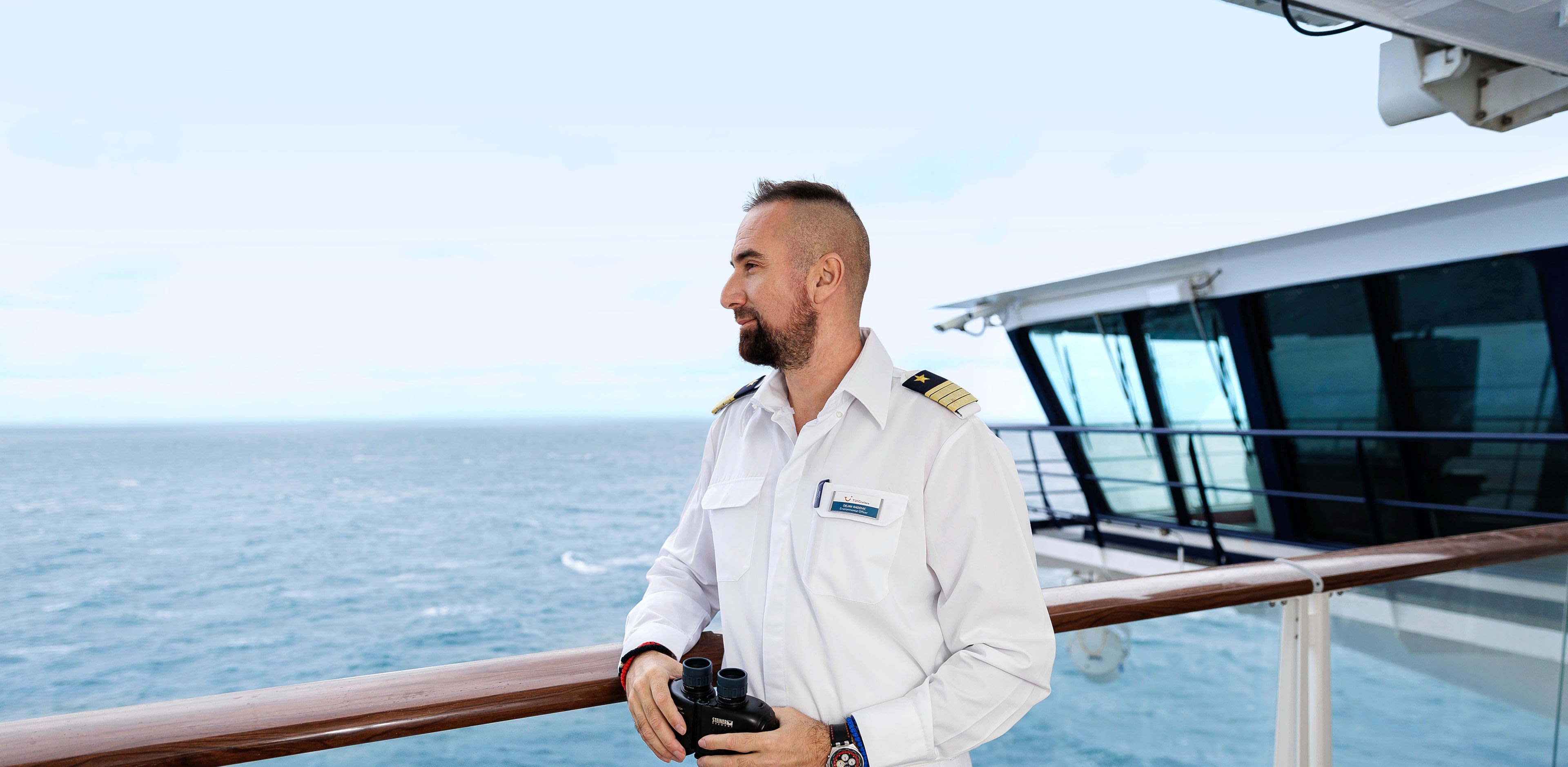 Nachhaltigkeit - Umweltoffiziere Mann in Uniform mit Fernglas auf Kreuzfahrtschiff der Mein Schiff® Flotte.