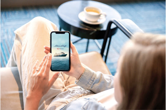 Person entspannt mit Smartphone, Kreuzfahrtschiff der Mein Schiff® Flotte, Kaffeetasse im Hintergrund. Person entspannt mit Smartphone, Kreuzfahrtschiff der Mein Schiff® Flotte, Kaffeetasse im Hintergrund.