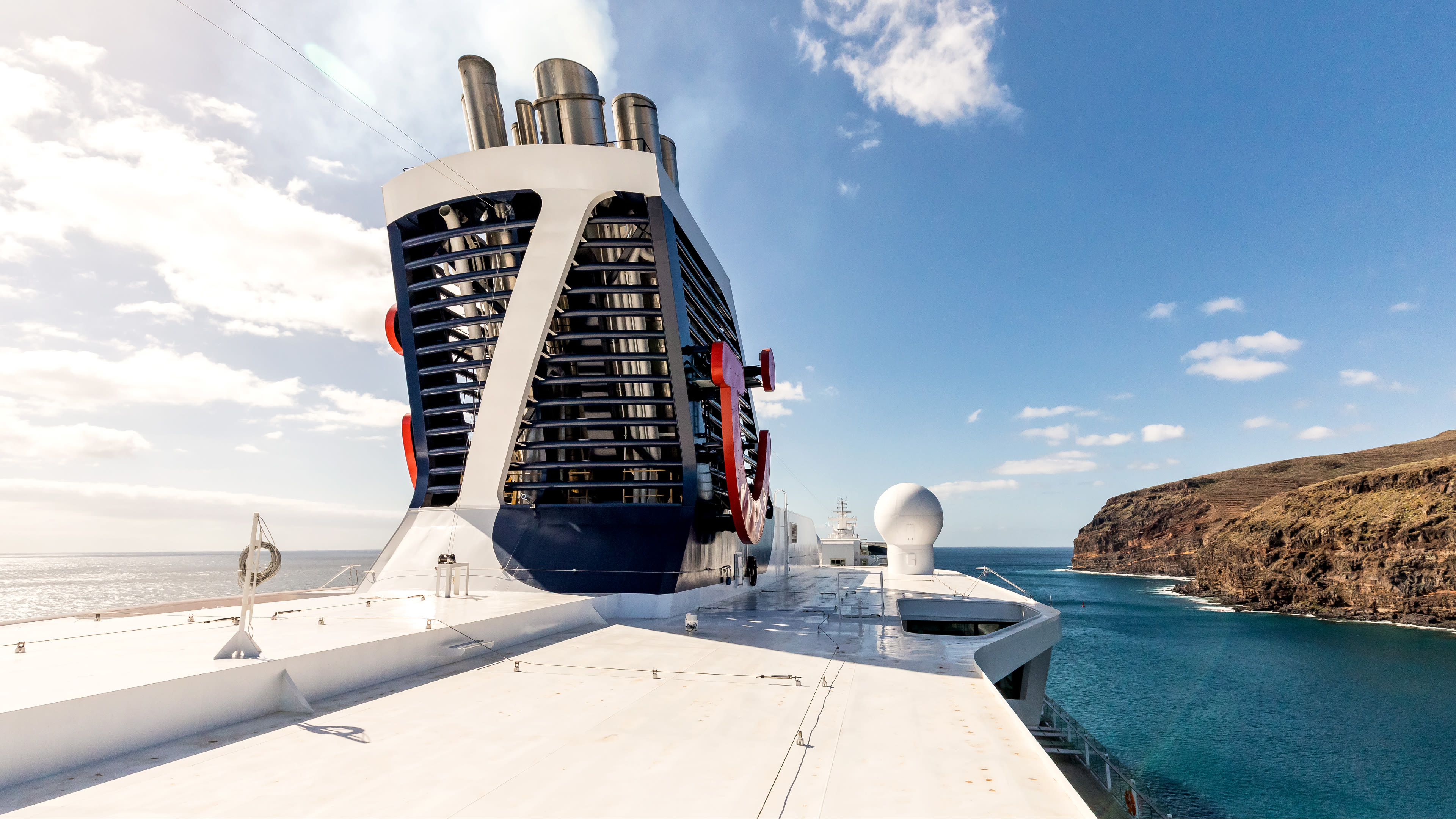 Kreuzfahrtschiff der Mein Schiff® Flotte vor felsiger Küste und blauem Himmel.