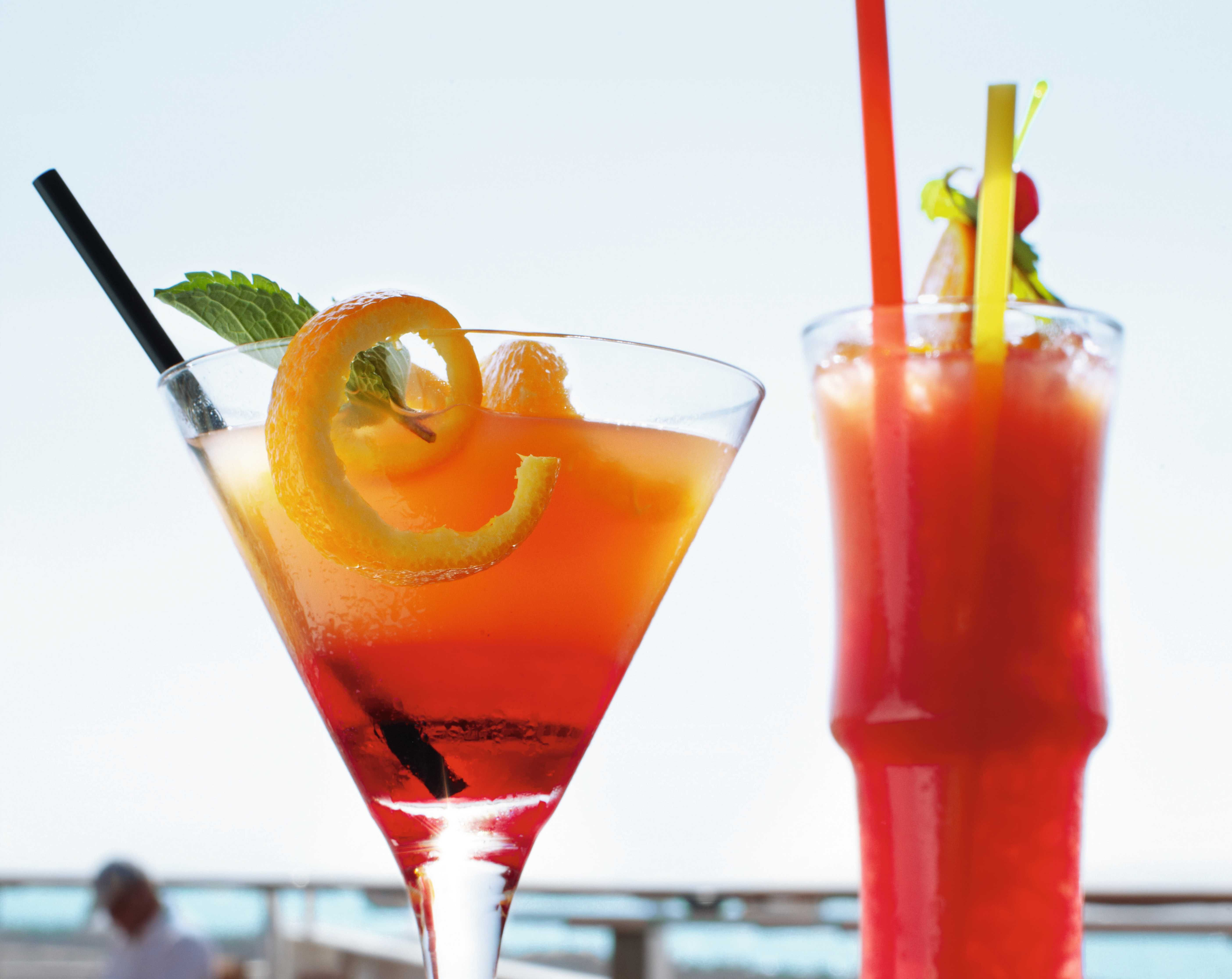 Zwei bunte Cocktails mit Strohhalmen vor blauem Himmel.