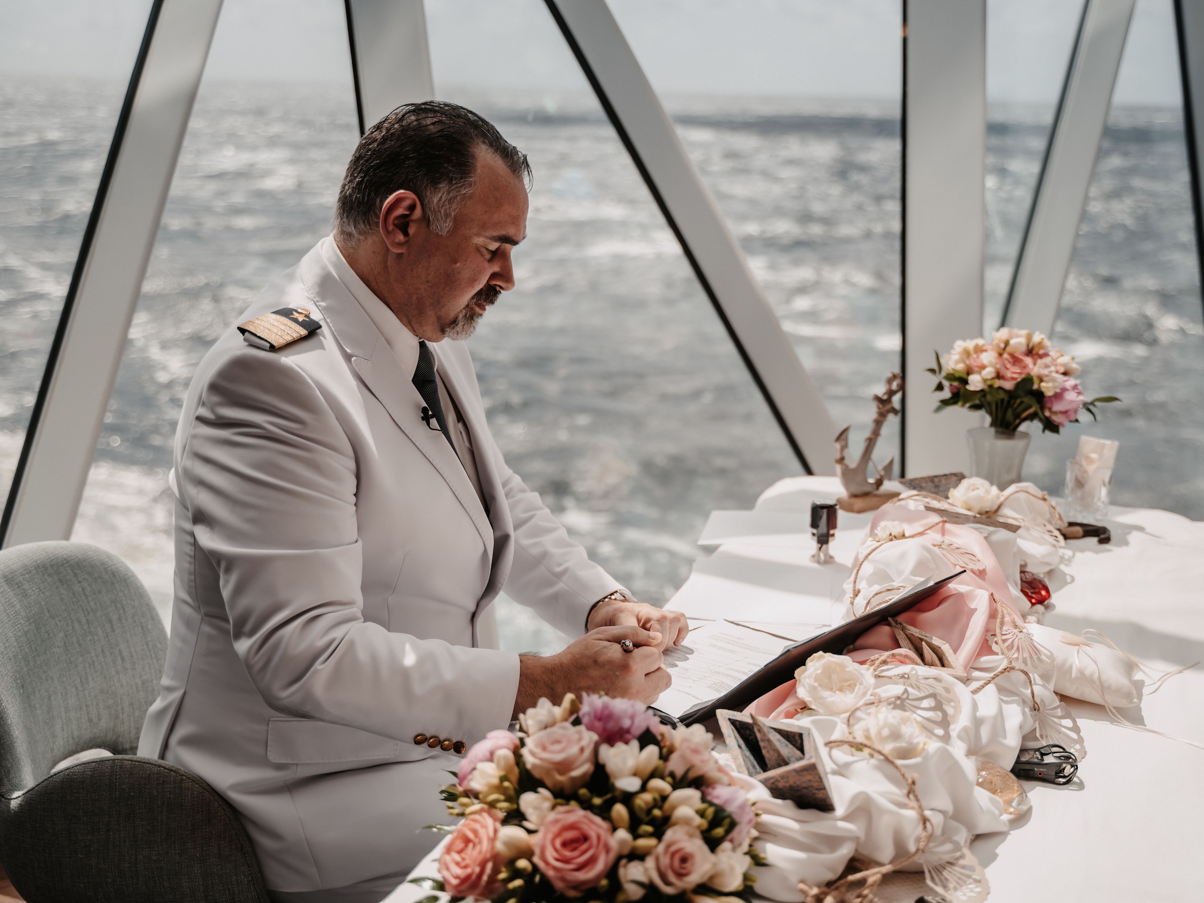 Trauung an Bord Kapitän in weißer Uniform bei Hochzeit auf Kreuzfahrtschiff, Blumenarrangement.