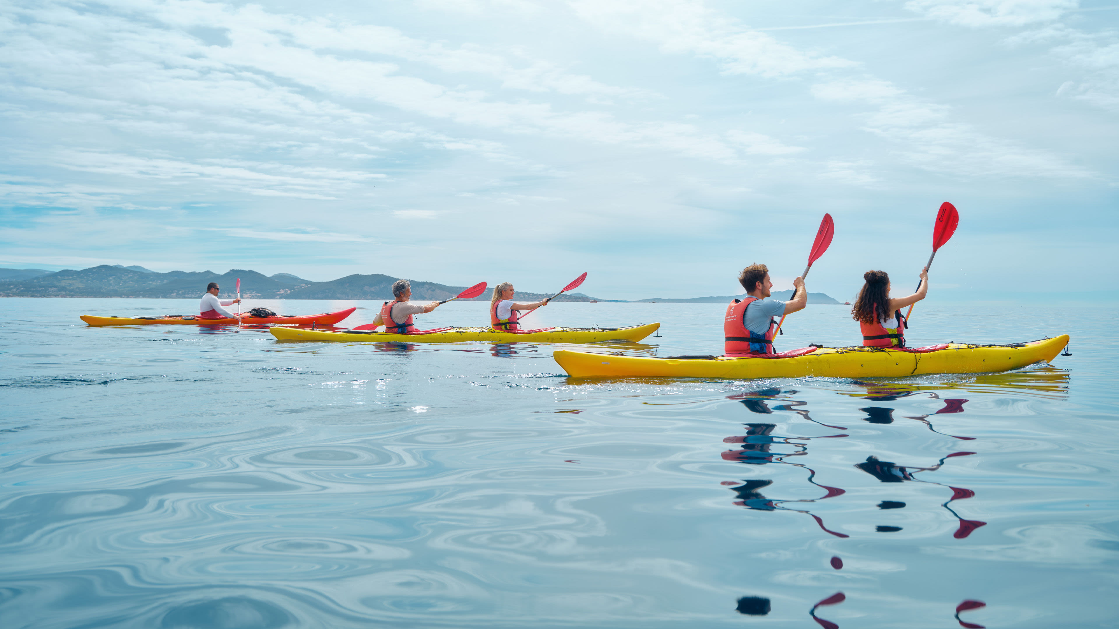 Menschen paddeln in gelben Kajaks auf ruhigem Meer.