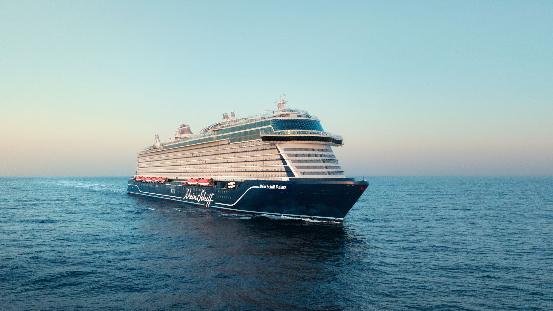 Kreuzfahrtschiff der Mein Schiff® Flotte auf offenem Meer bei Sonnenuntergang.