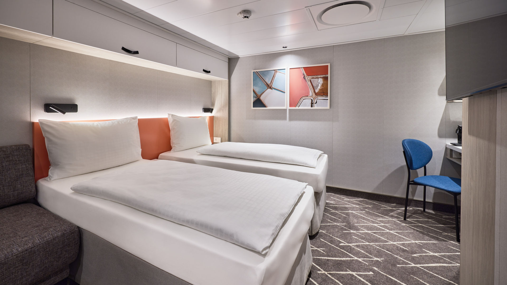 Helles Kreuzfahrtschiff-Kabine mit zwei Betten, blauer Stuhl.
