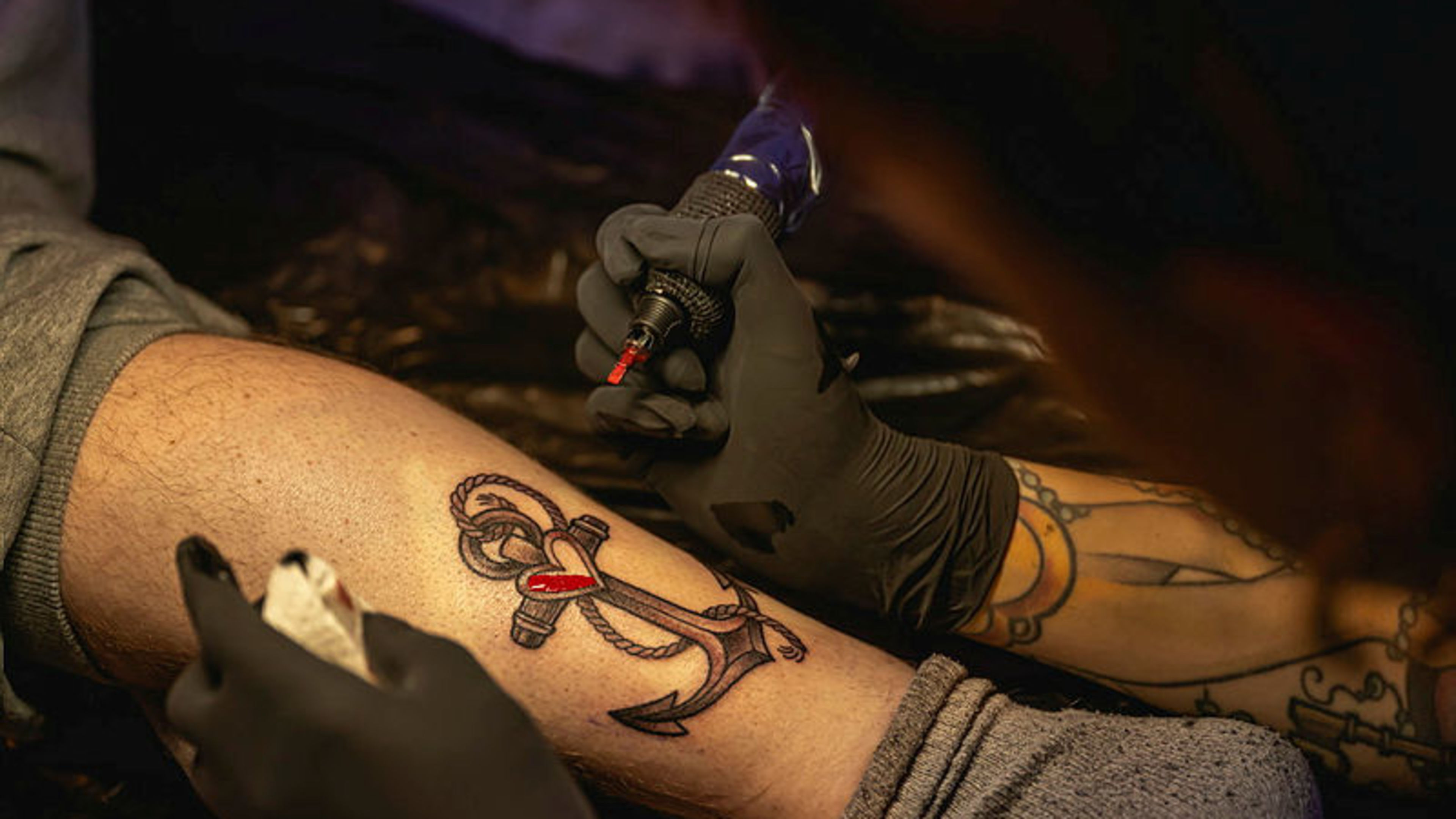 Wildcat Tattoo Cruise Tätowierer sticht Anker-Tattoo mit Herz auf Bein.