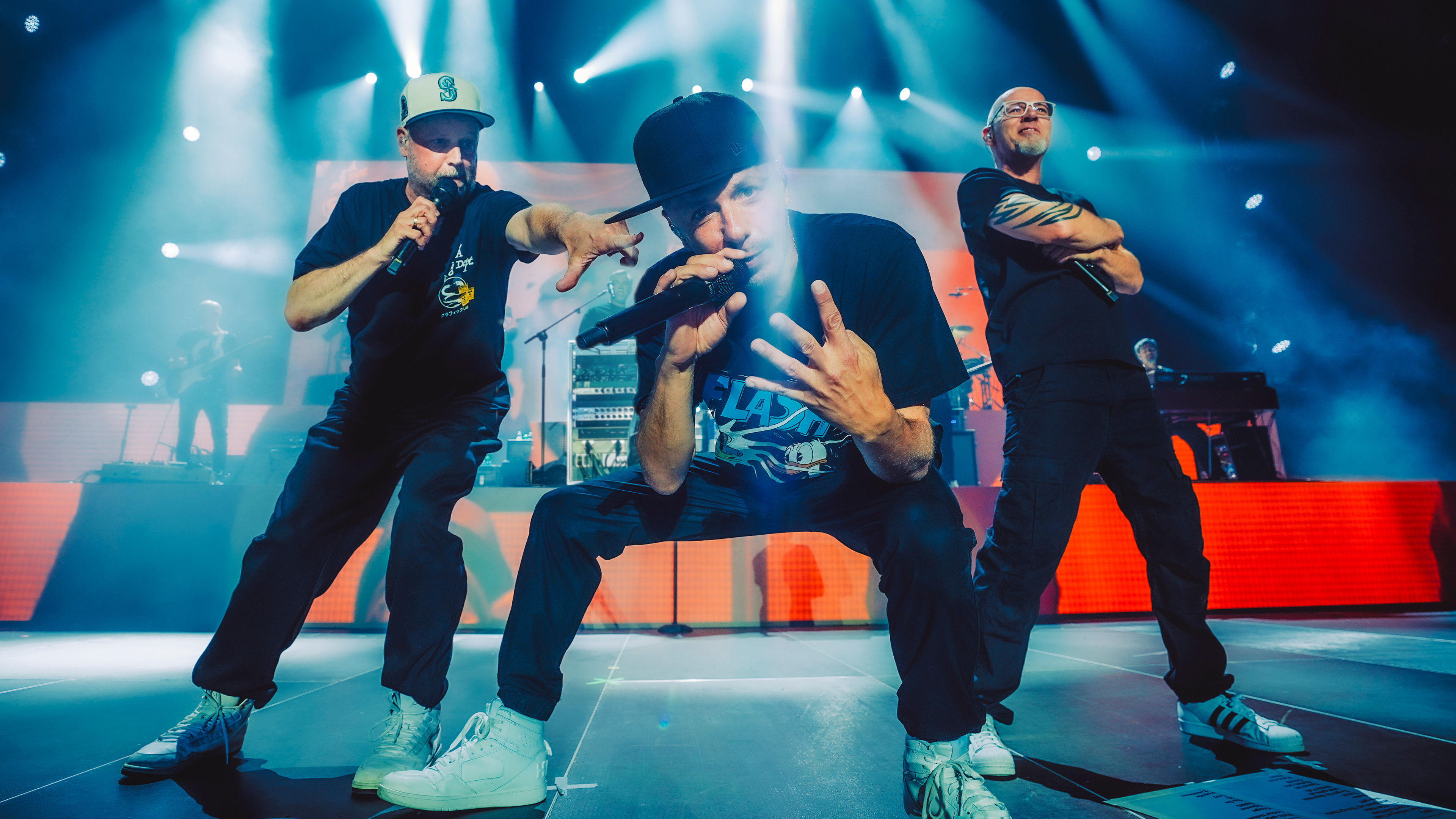 Drei Männer performen auf einer Bühne mit blauen Lichtern.