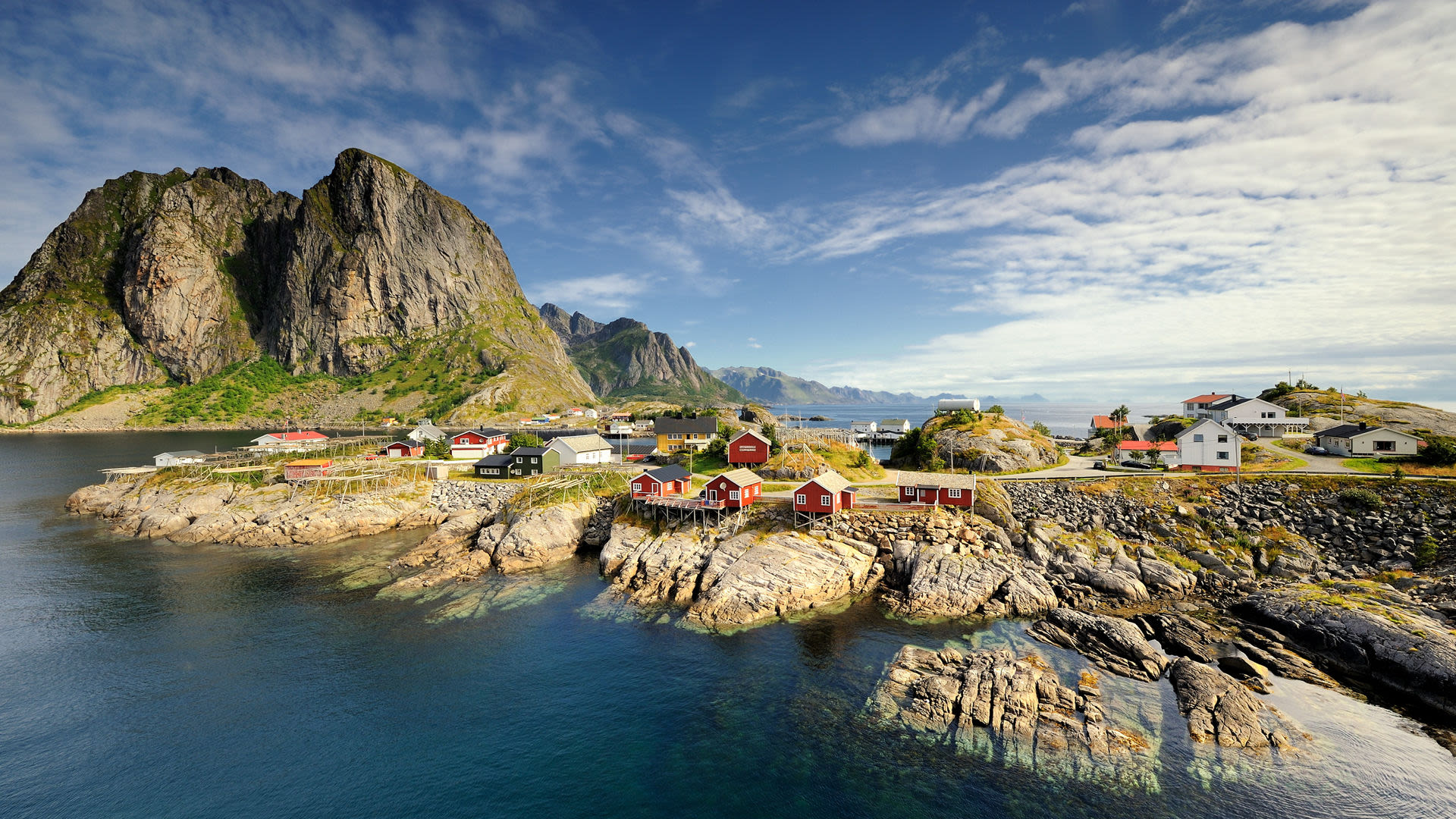 Bunte Häuser auf Lofoten-Inseln vor majestätischen Bergen und blauem Himmel.