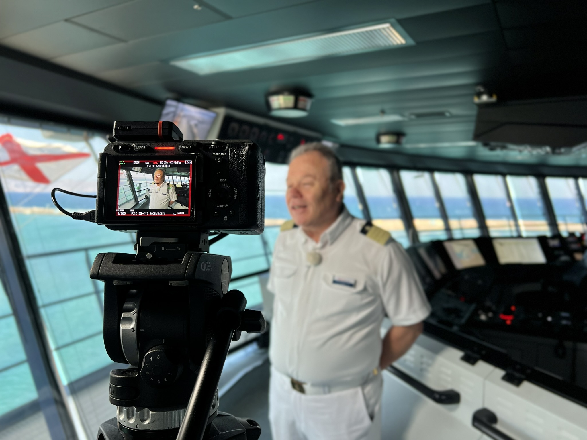Kapitän in weißer Uniform auf Kreuzfahrtschiffbrücke, Kameraaufnahme.